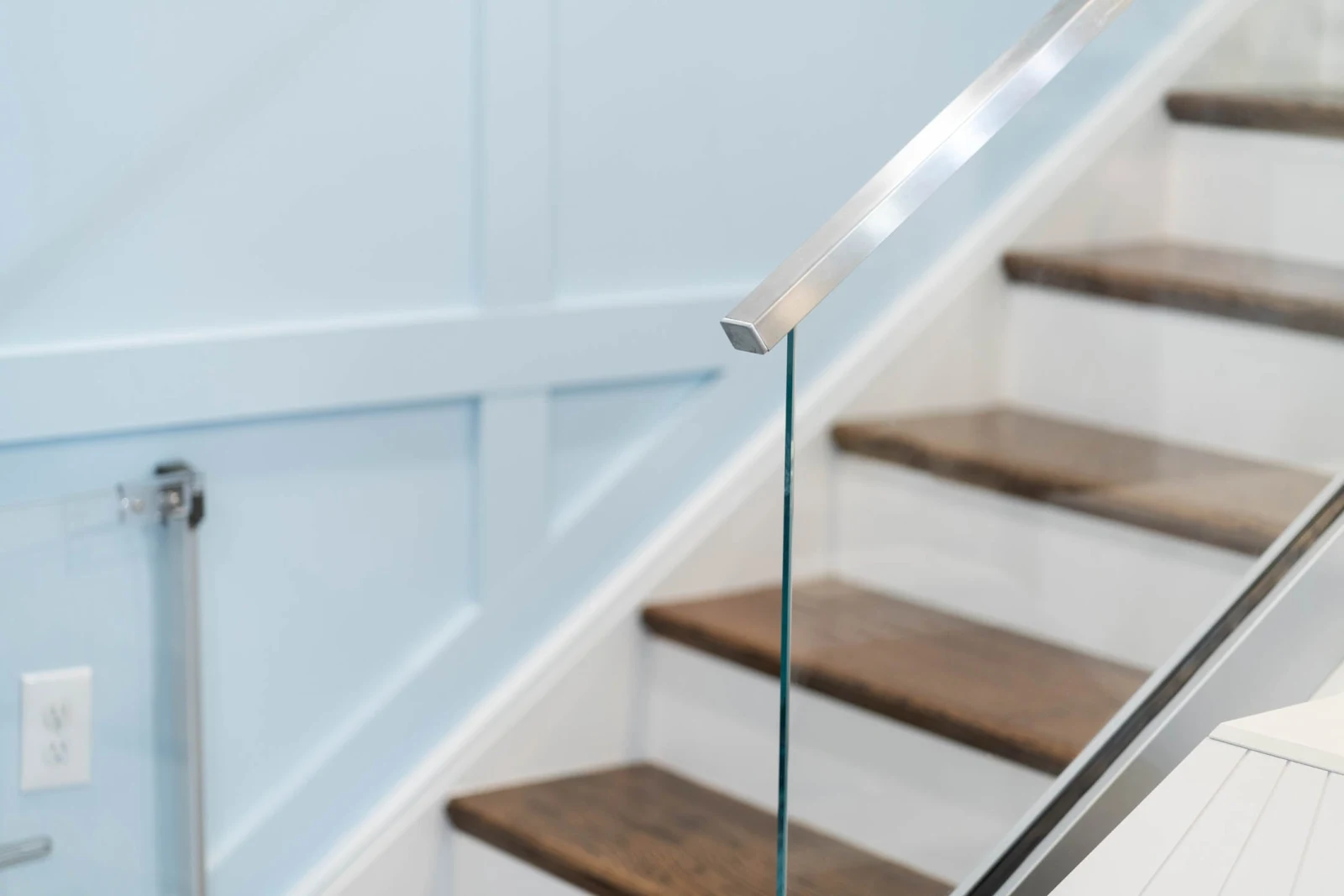 Detail of a stainless top rail ending above glass beside wood stair treads