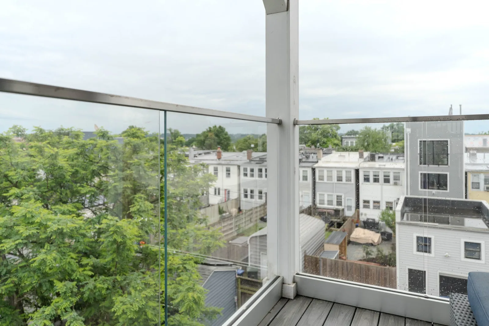 Outdoor balcony with frameless glass railing looking over rooftops and treetops