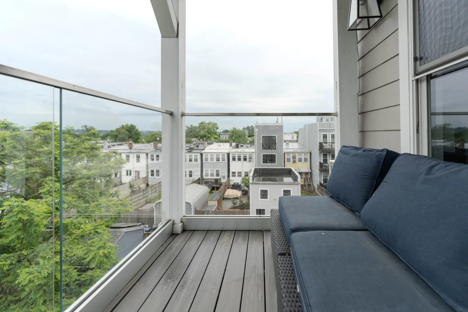 Covered balcony with a blue sectional beside glass railing and a neighborhood view