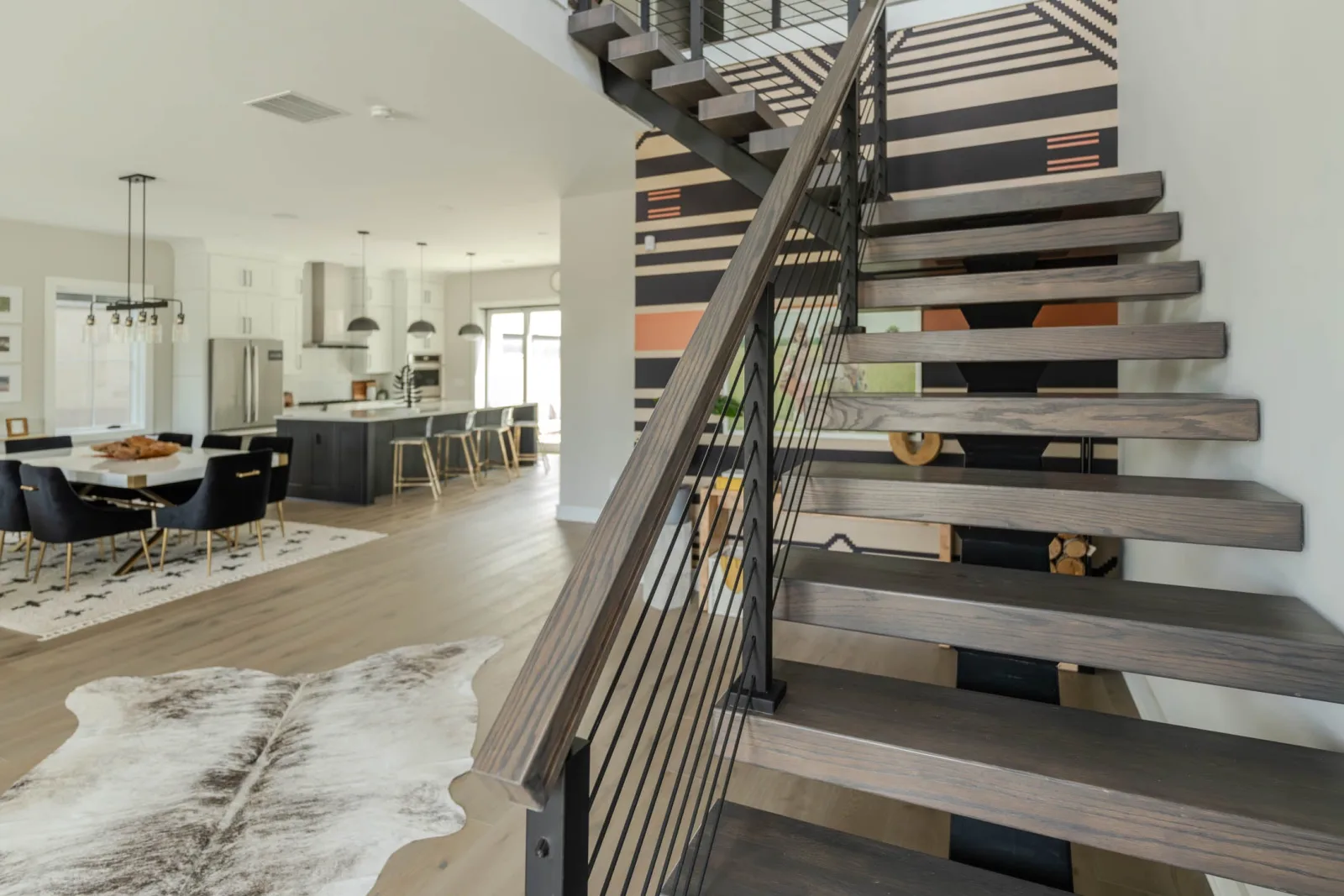 Floating stair with rod railing and wood handrail rising past a striped painted wall
