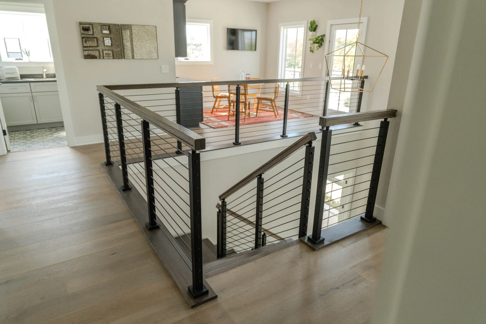 Rod railing wrapping the stairwell opening beside kitchen and plank flooring