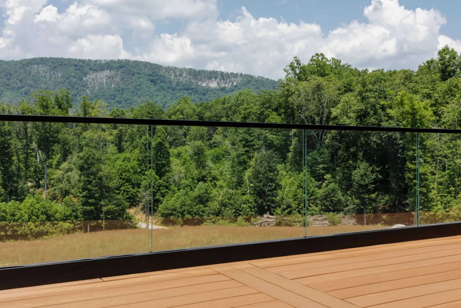 Frameless glass railing along a deck opening onto forested ridges and summer sky