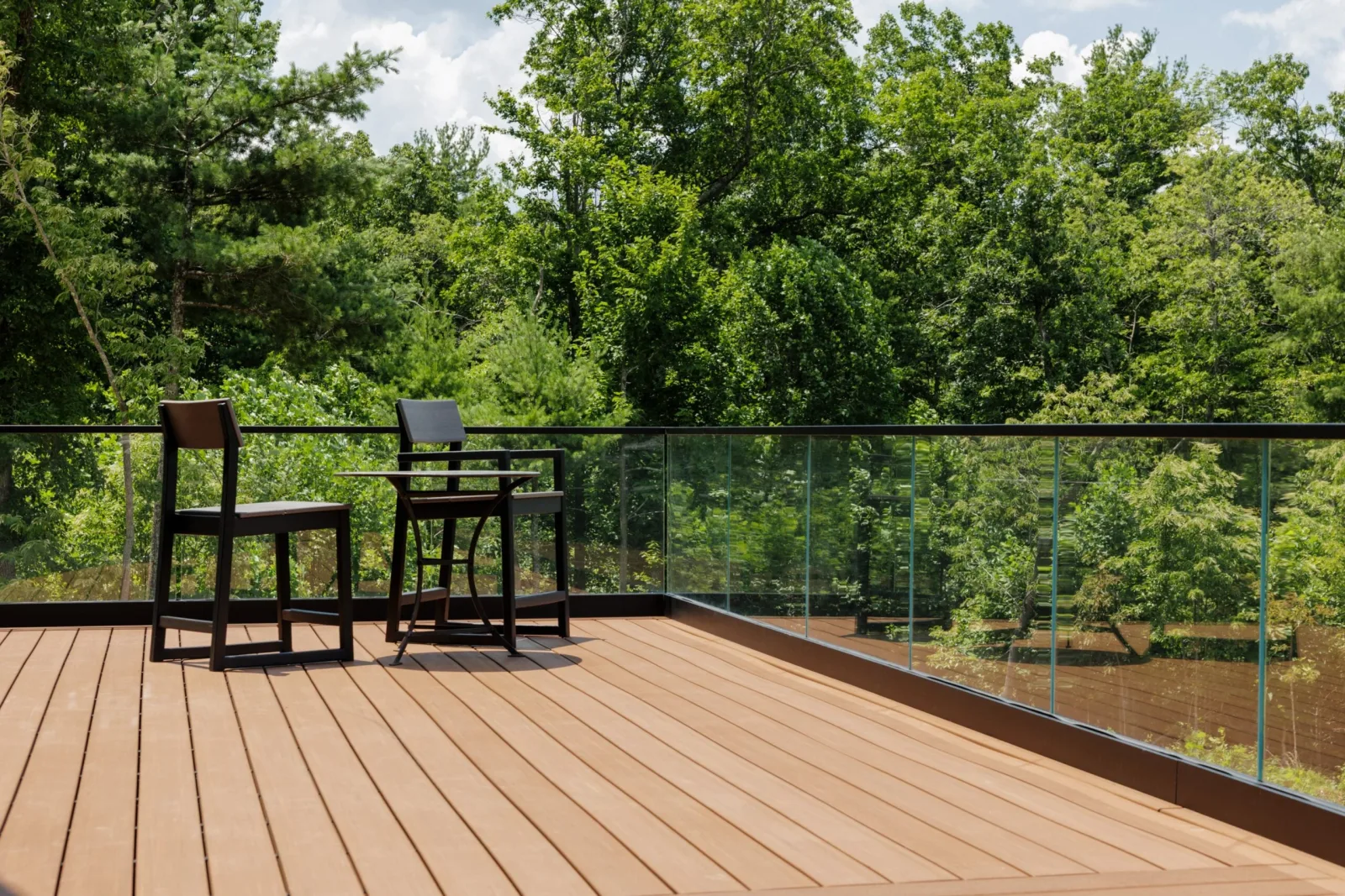 Two chairs and a bar table on the deck ringed by glass railing
