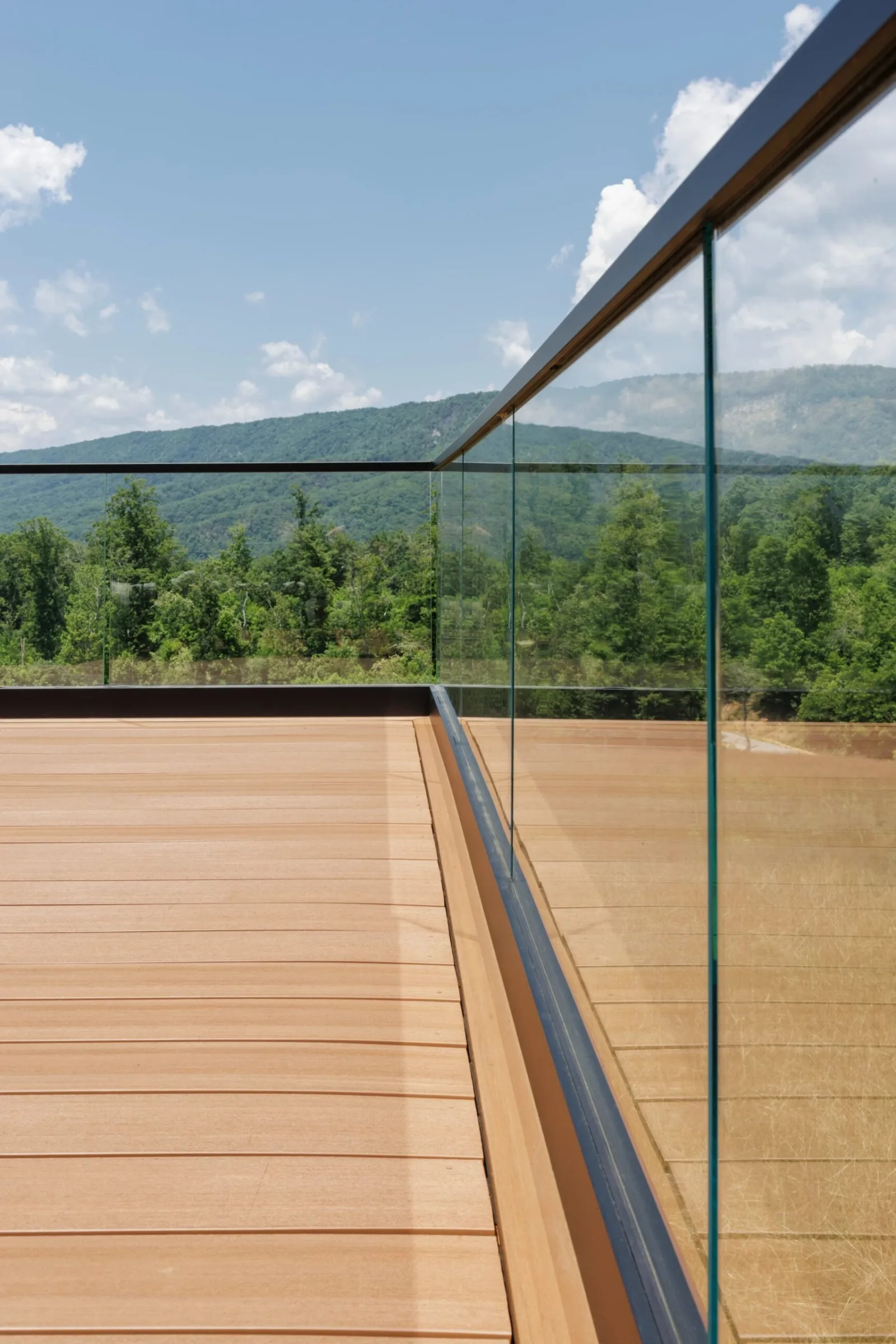 Glass panels running the deck edge with mountain ridge beyond warm boards