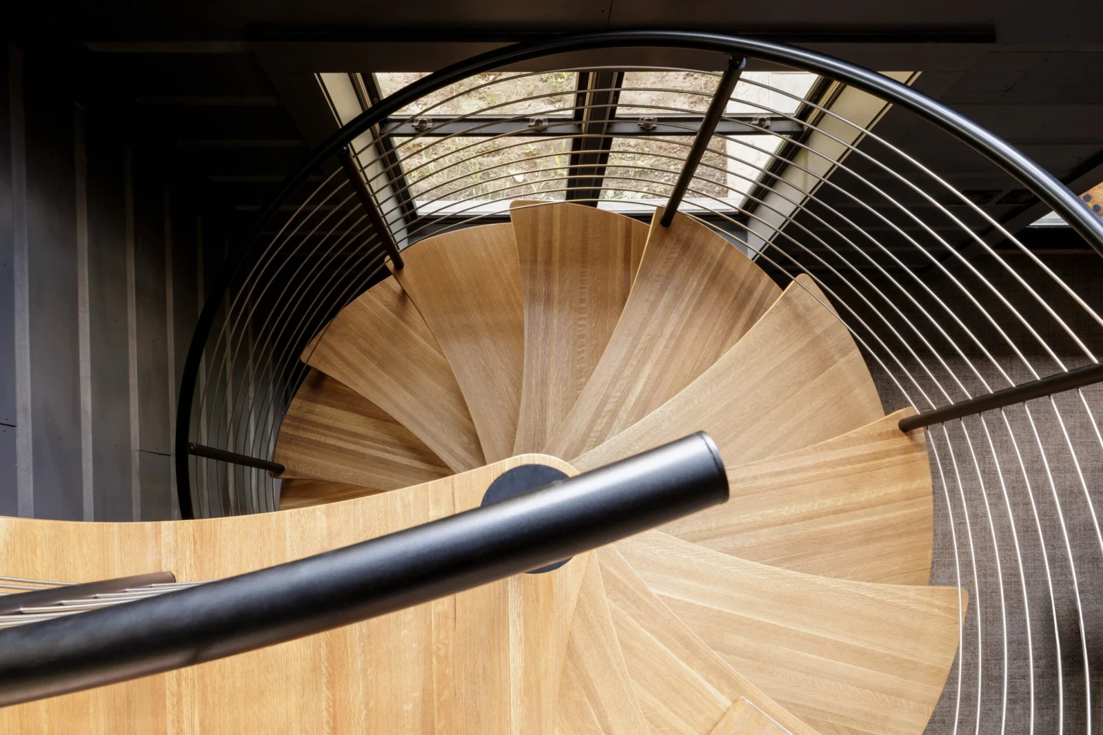 Spiral stair from above, wood treads fanning from a black column inside cable railing