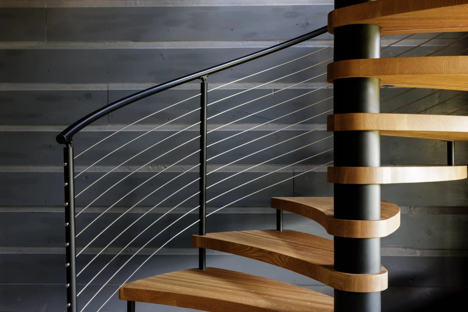 Curved handrail and taut cables following the spiral past dark board walls