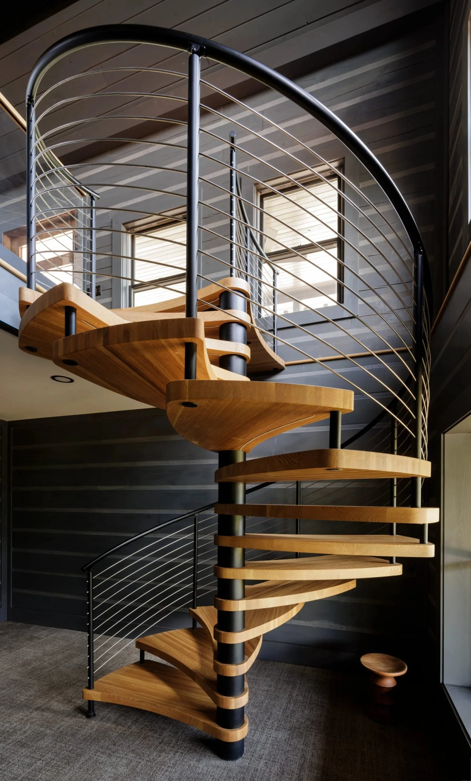 Spiral stair with wood treads and curved rod railing in a dark board-lined room