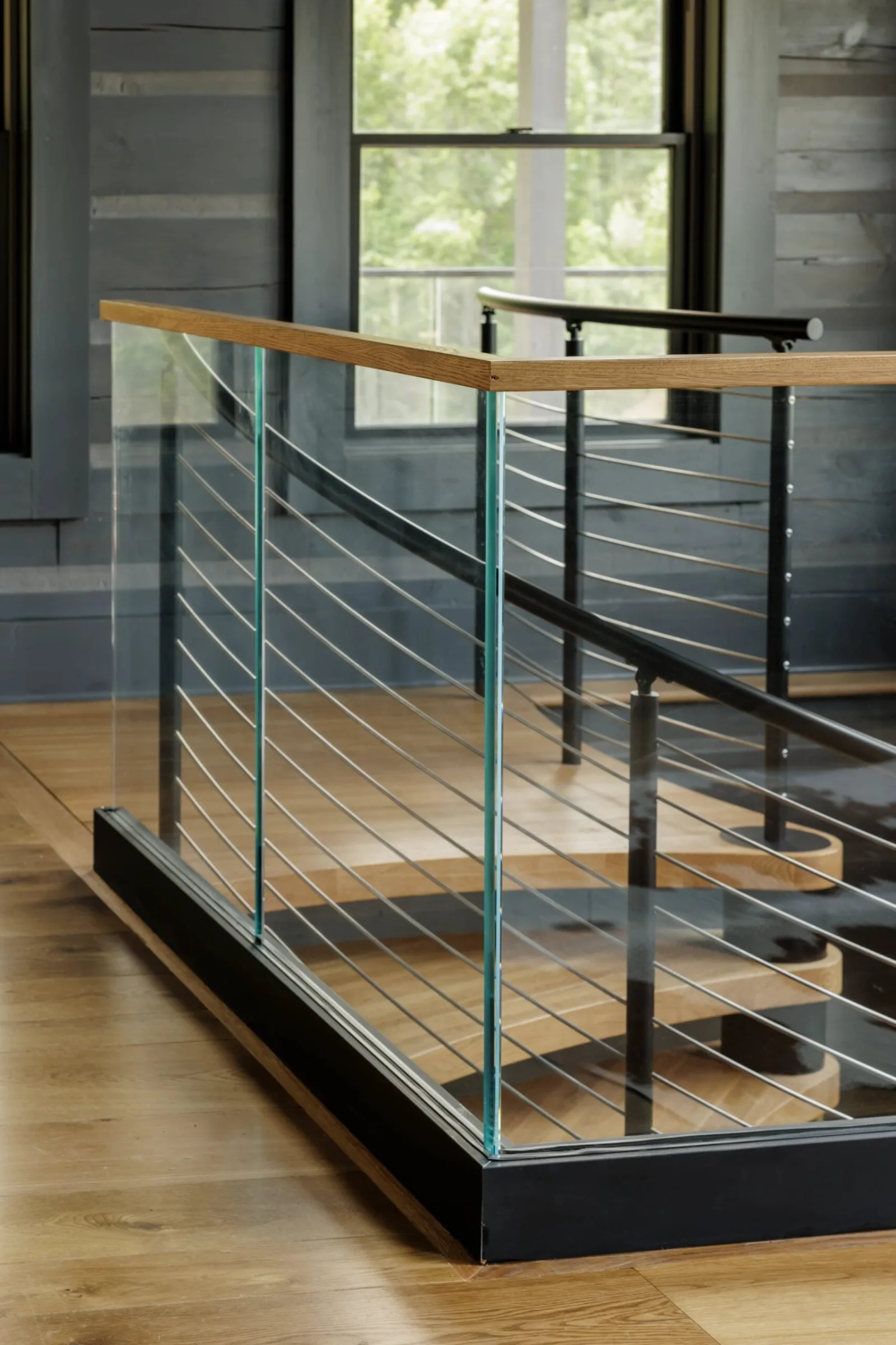 Glass panels with a wood top rail enclosing the stair opening beside a window