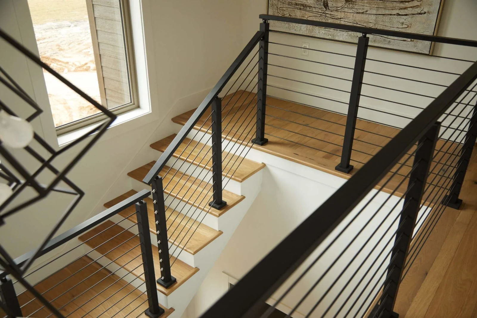 Looking down on black posts and horizontal rods framing a stairwell with wood treads