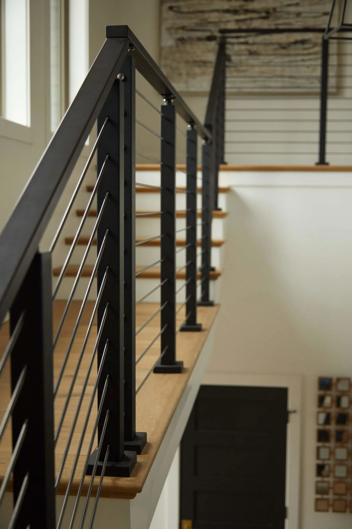 Detail of a balcony run with black posts, horizontal rods and a wood top rail