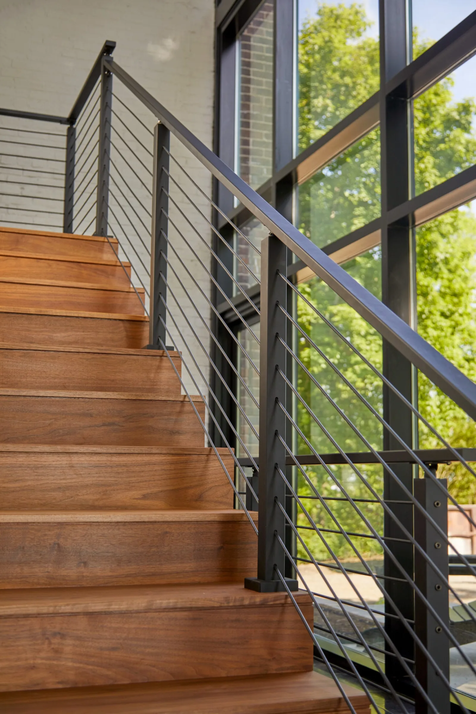 Wood treads rising beside a rod railing and a full-height window wall