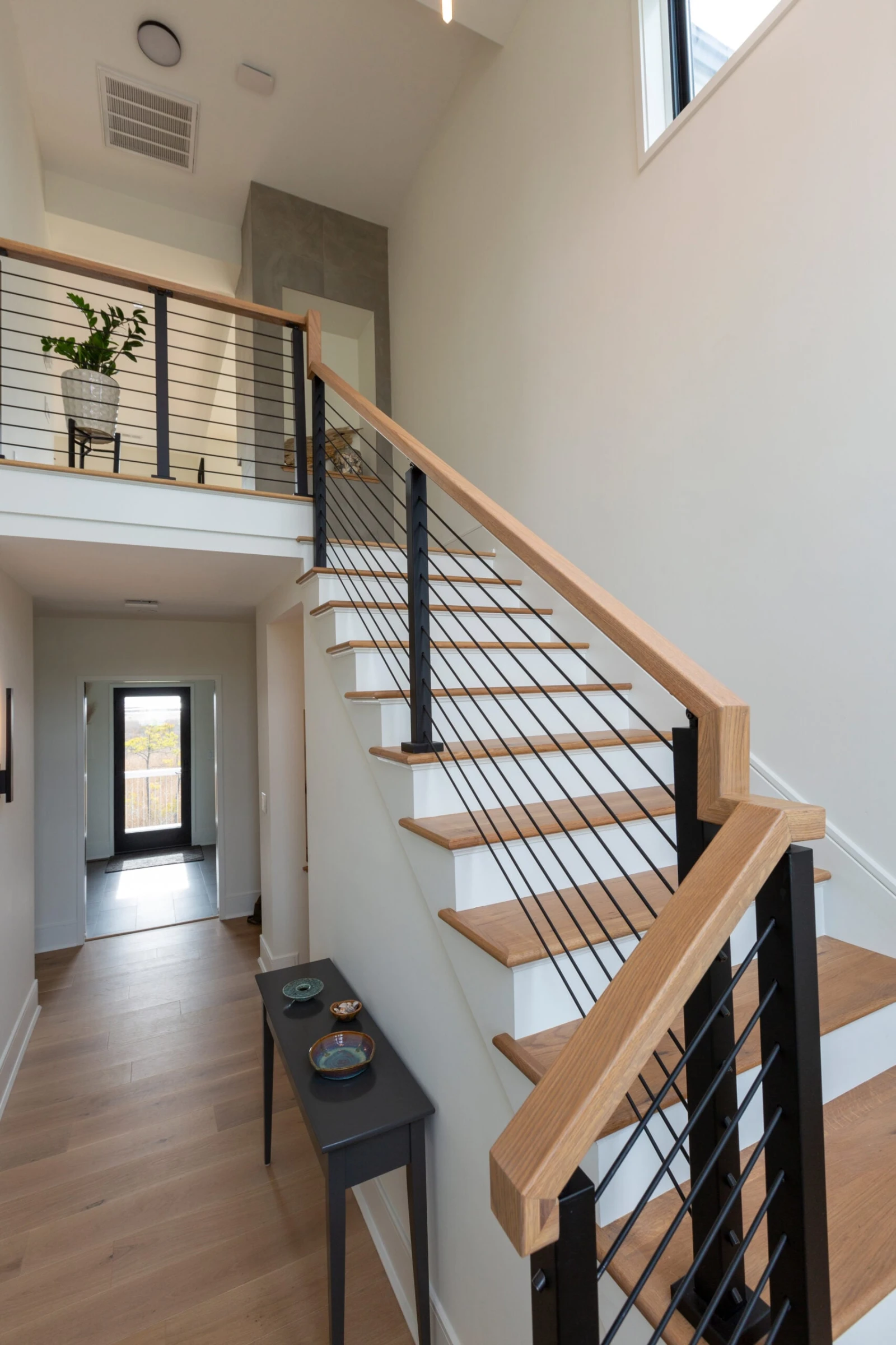 Wood-tread stair with black rod infill and wood top rail beside an open entry