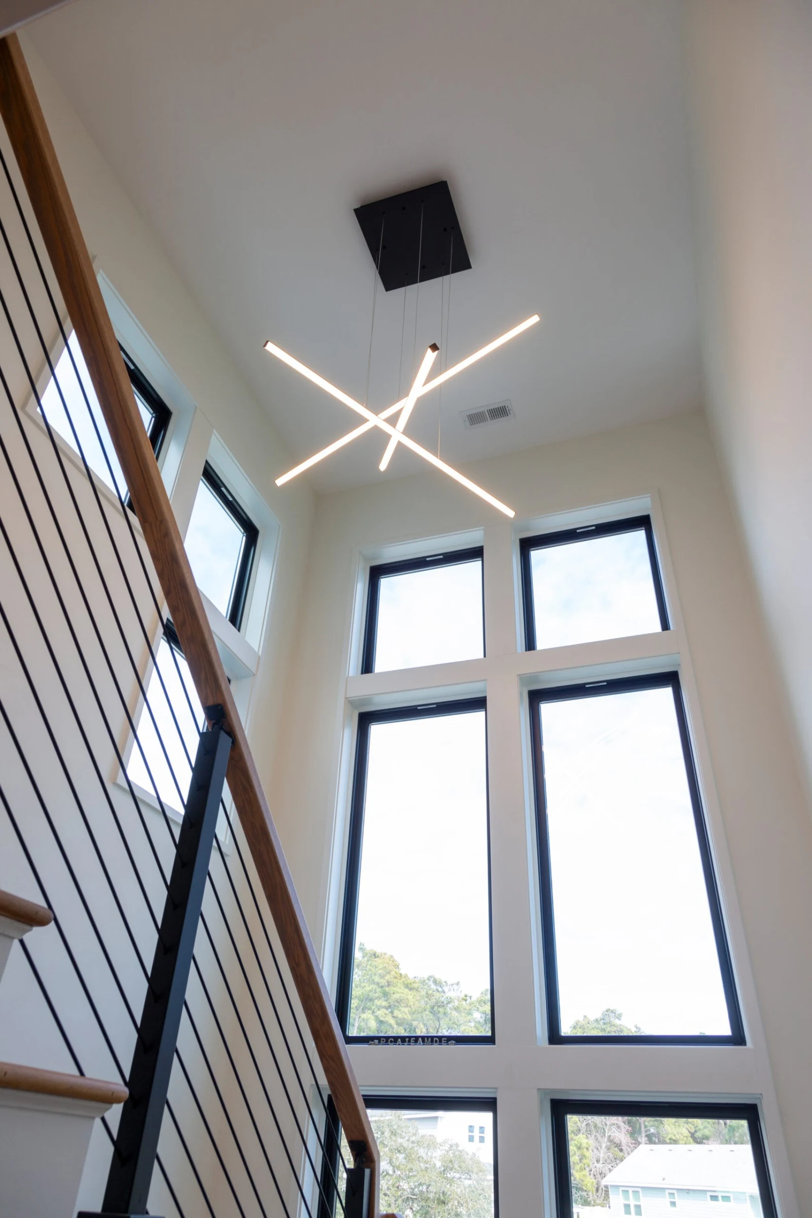 Looking up a two-story stairwell past black rod railing to tall windows