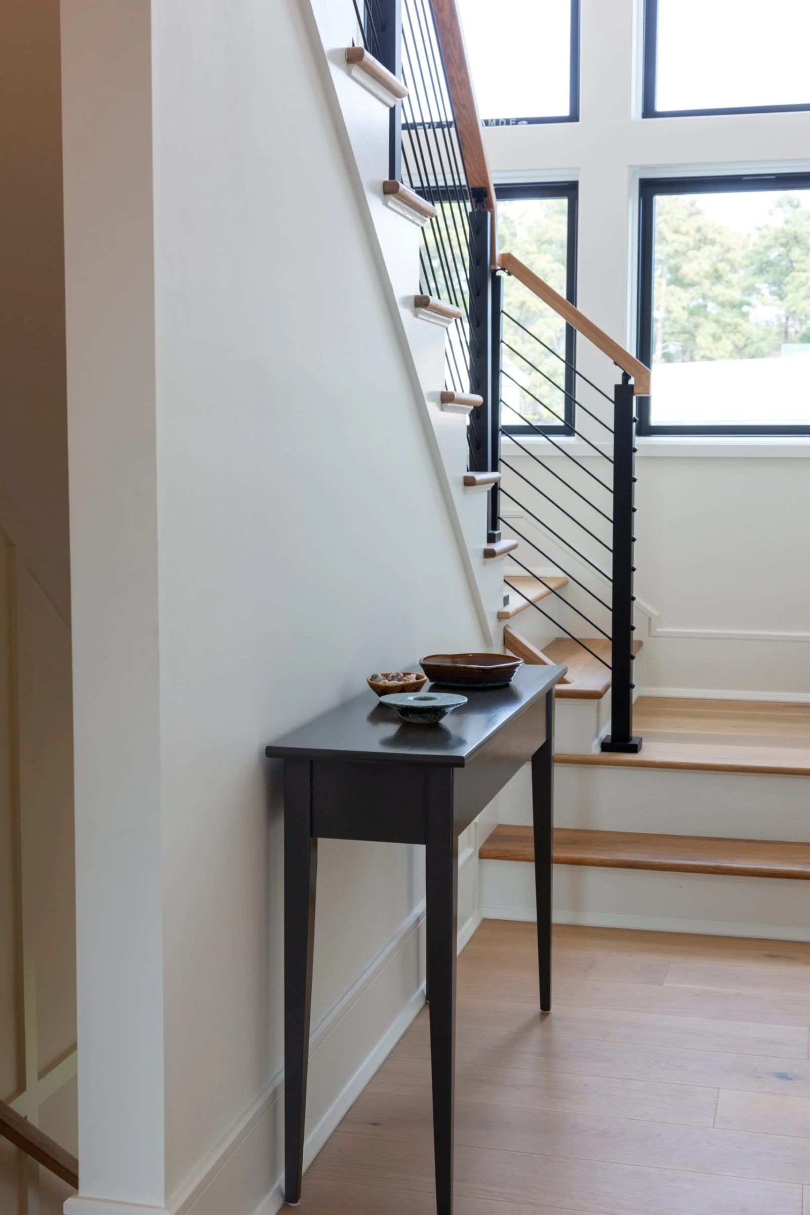 Console table in a hallway with a black rod railing and light handrail climbing behind