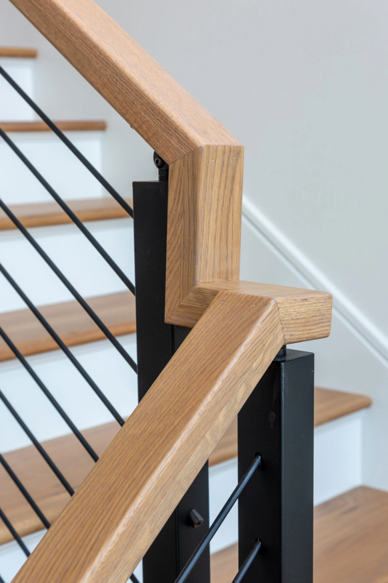 Close view of a wood top rail mitered at a black post above the treads