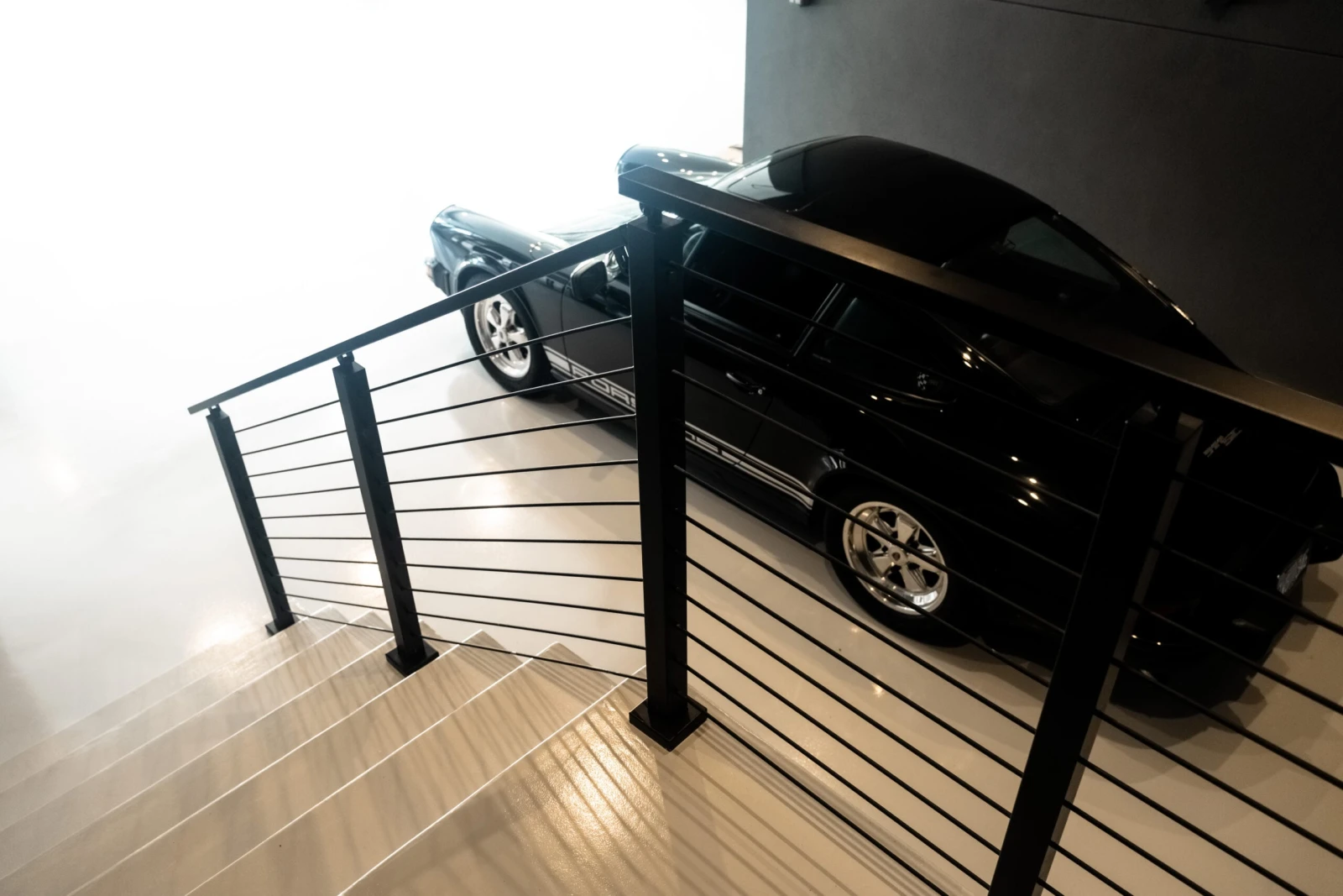 Overhead view of a black rod railing guarding stairs above two parked cars