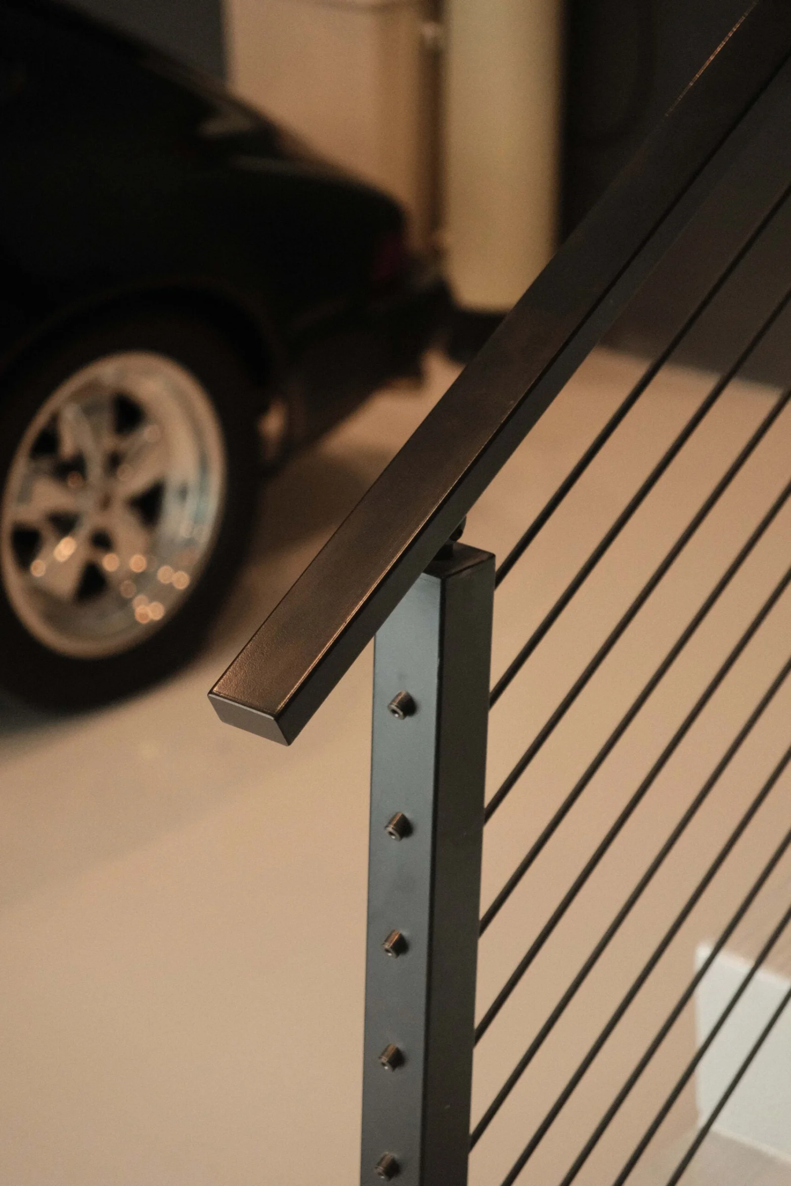Black railing post and rods framing a parked sports car in a polished garage