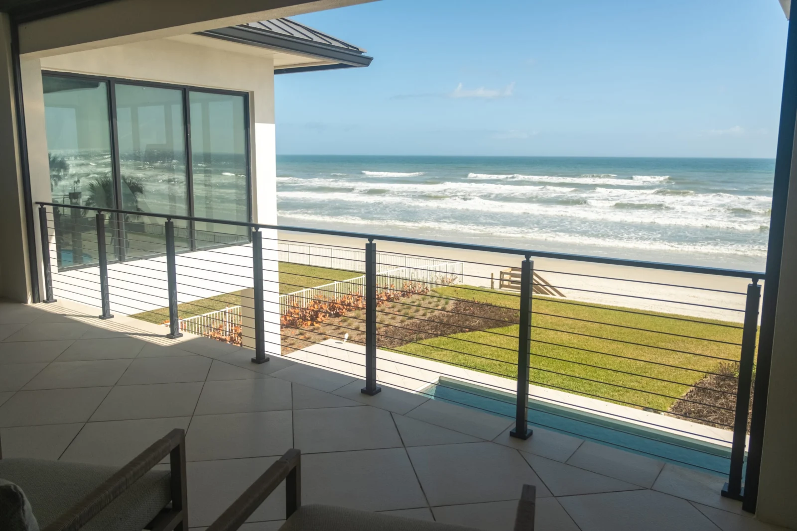 Covered tiled balcony with black rod railing looking straight out at breaking surf