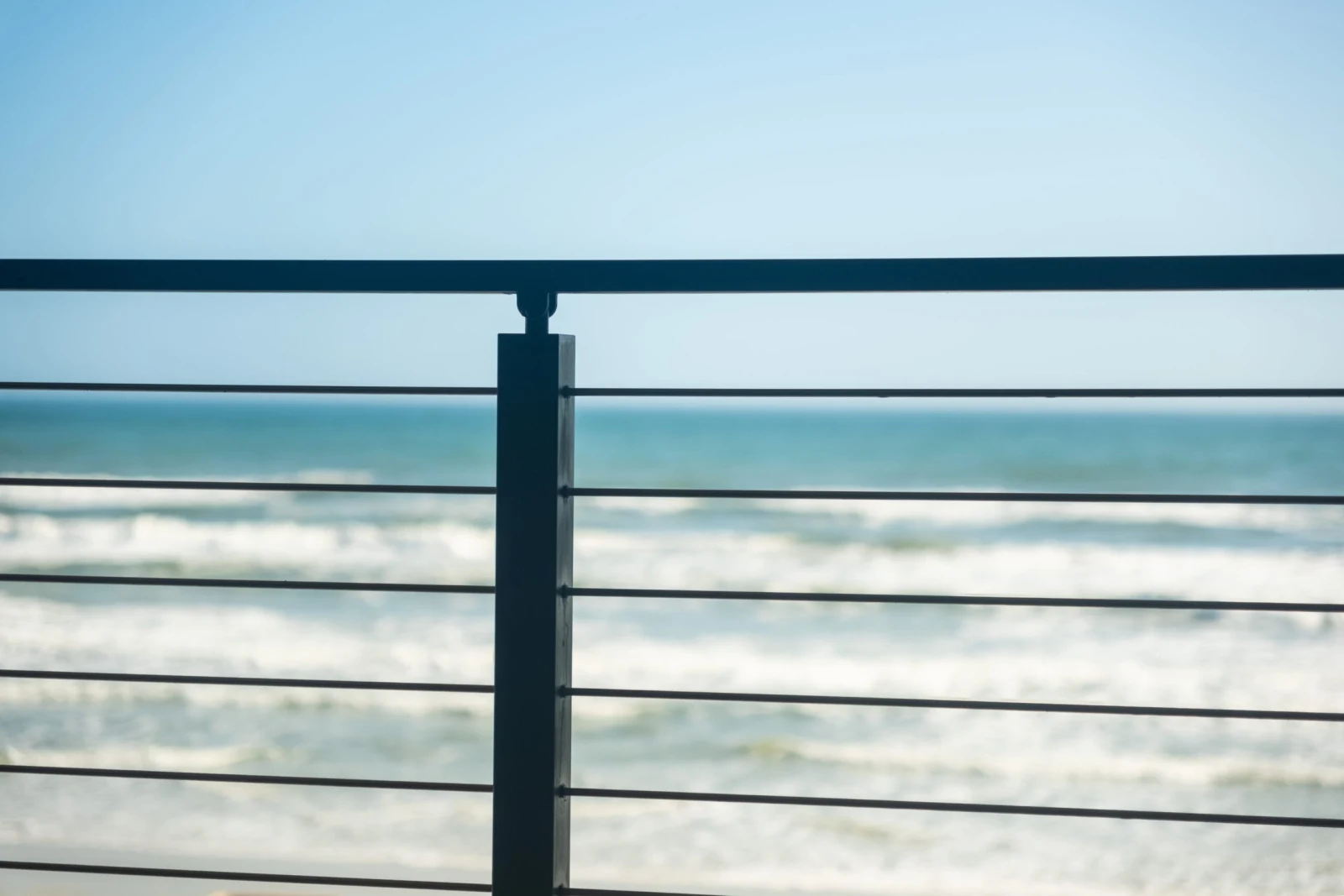 Single black post and horizontal rods silhouetted against breaking waves and open sky