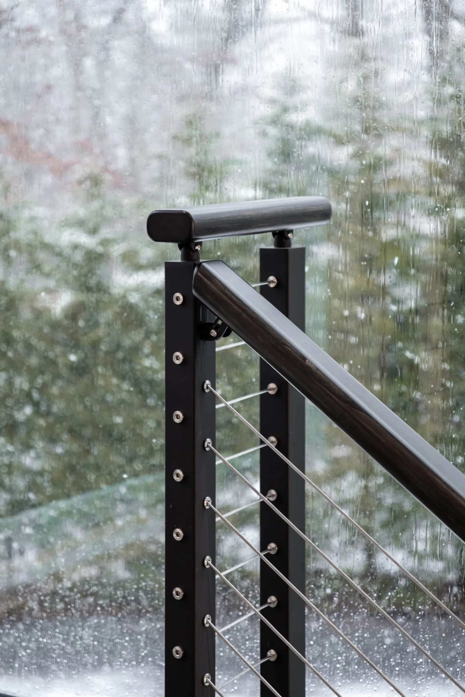 Rounded handrail cap on a black post as snow falls beyond the window