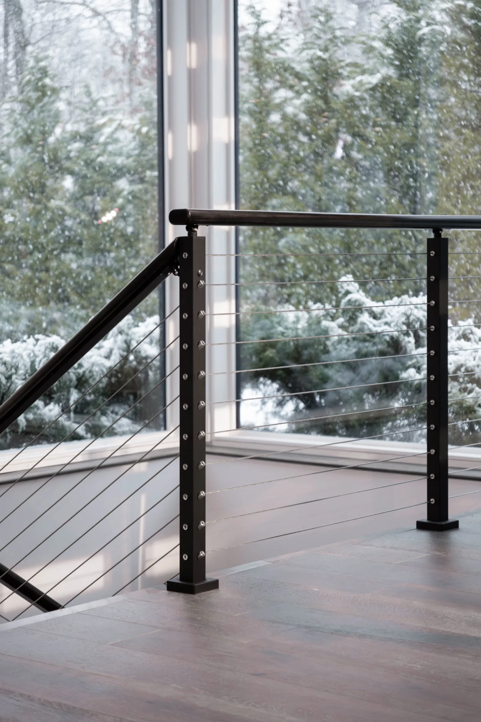 Black posts and cables at a landing corner with snowy woods through glass