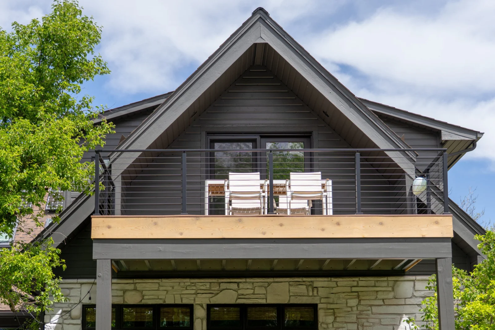Gabled dark house with an upper deck of black rod railing and white chairs