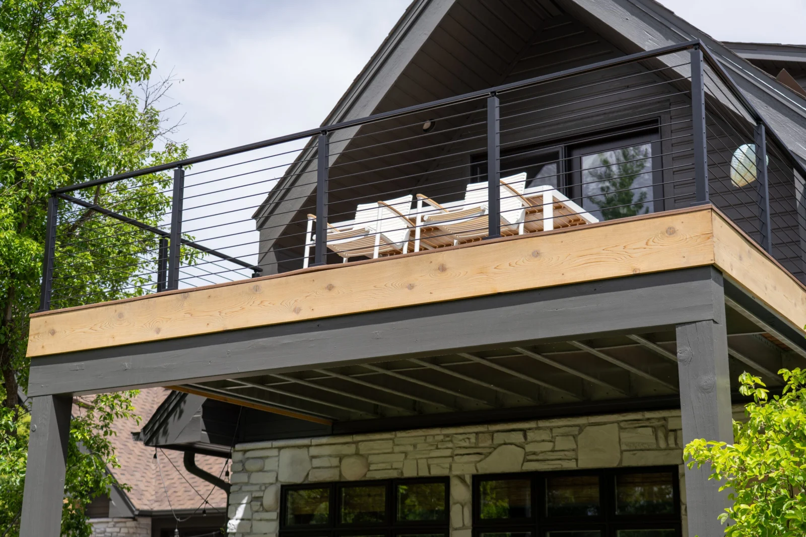 Elevated deck with black rod railing and seating above a stone-clad porch