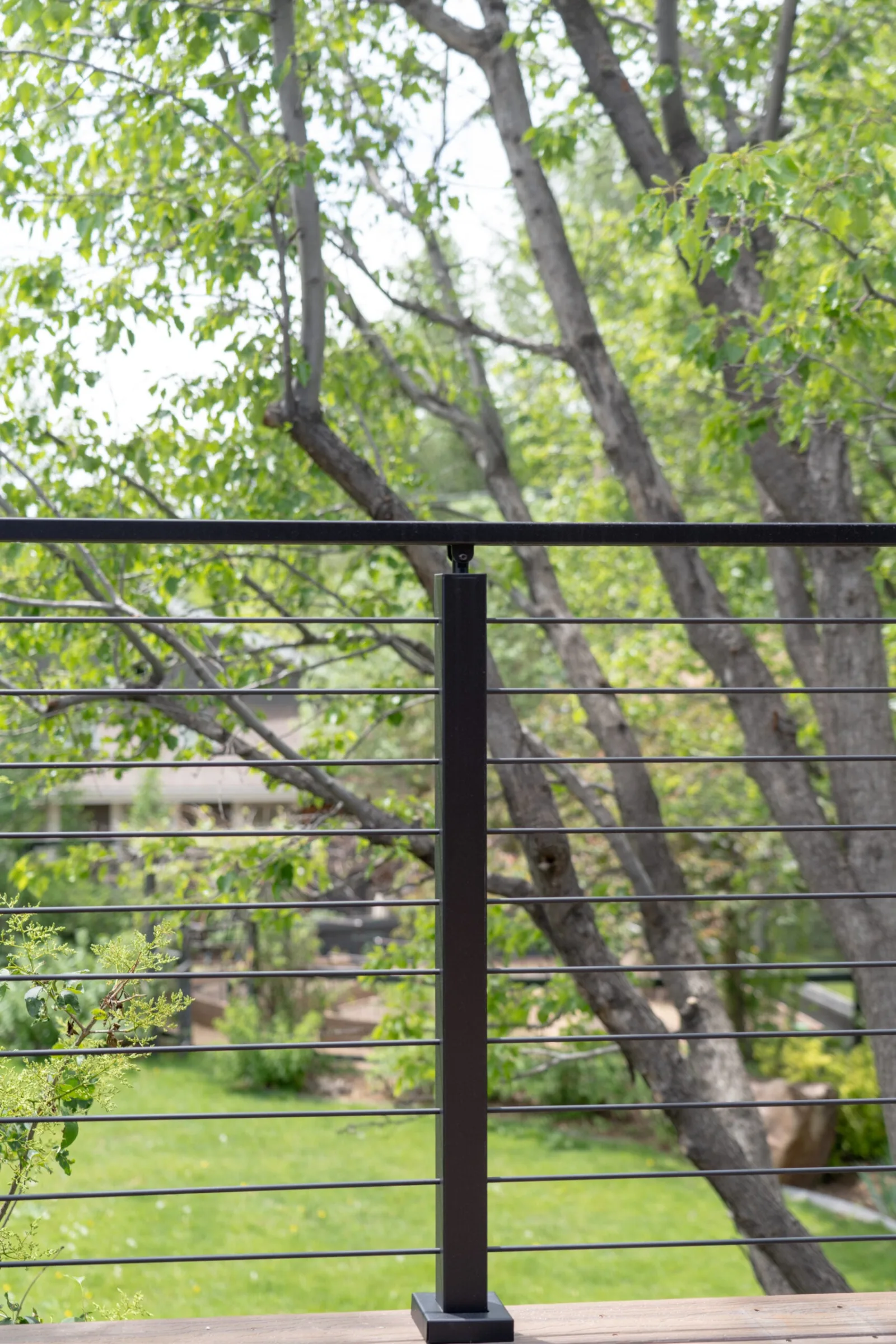 Single black post and horizontal rods framing a backyard of trees and lawn