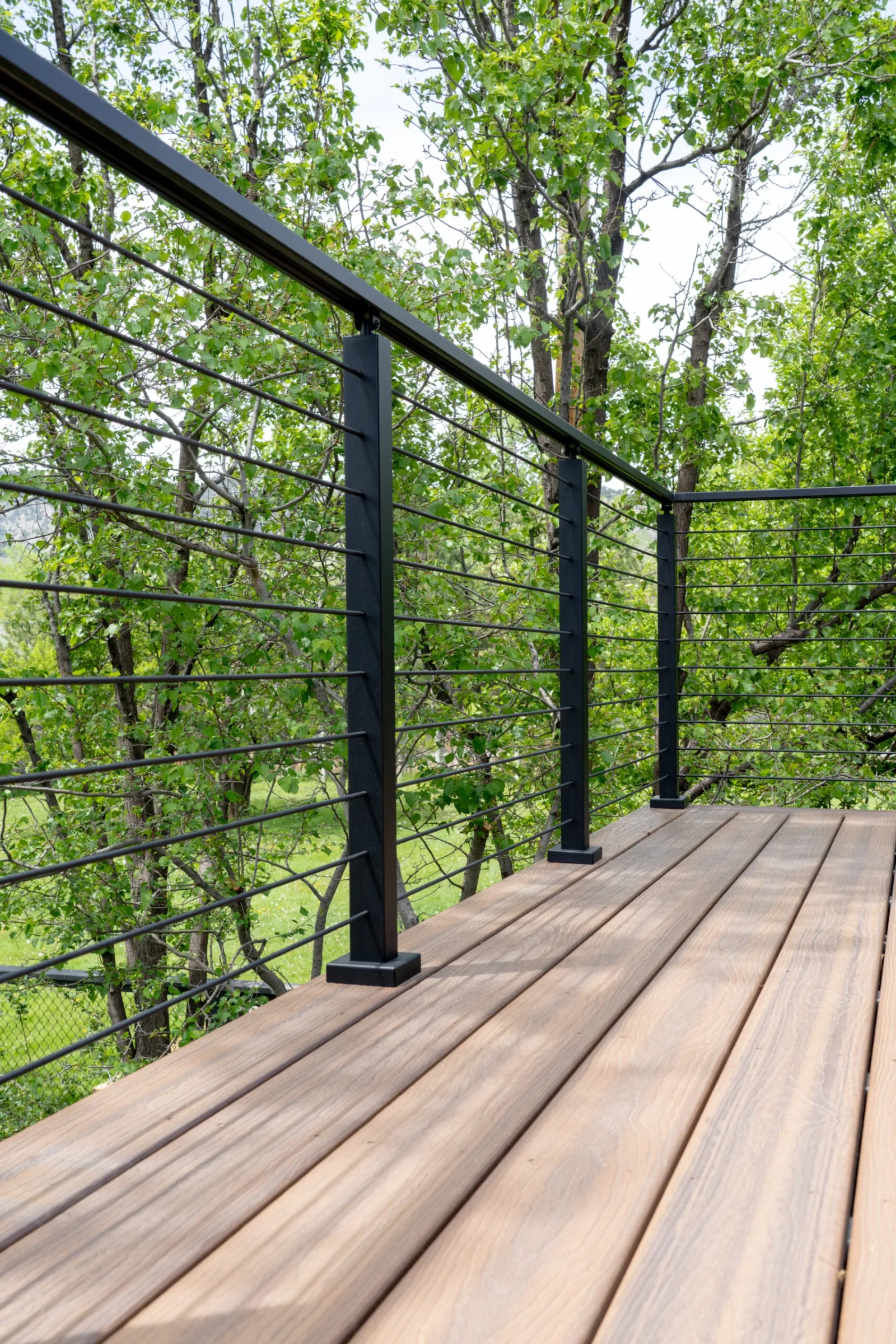 Perspective down a rod-railed deck with warm wood boards and dense greenery
