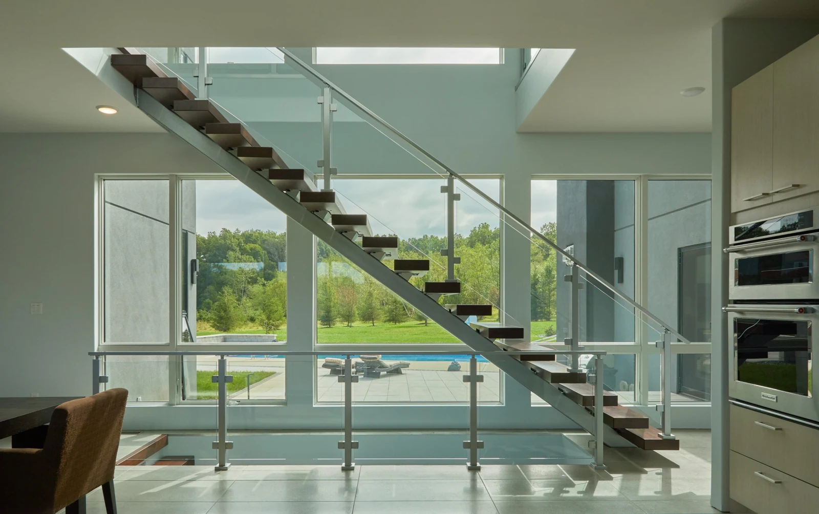 Floating treads crossing a two-story window wall above glass railing on slim posts