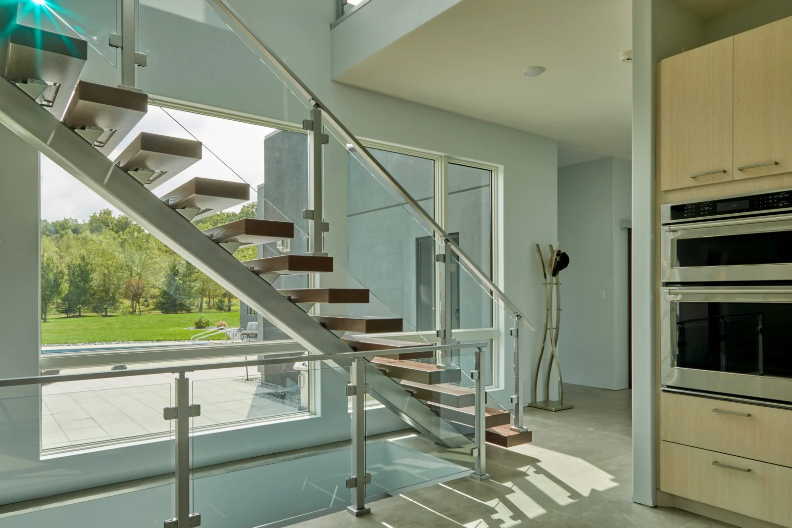 Stair seen from the kitchen, glass panels and silver top rail framing the lawn beyond