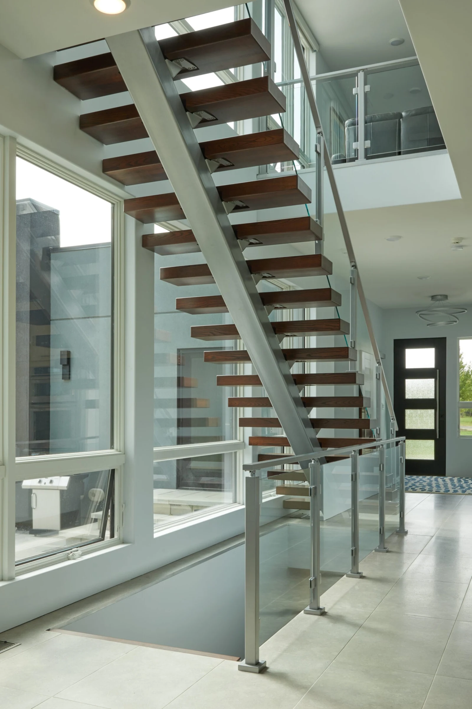 Straight floating stair with dark wood treads on a silver center stringer beside tall windows