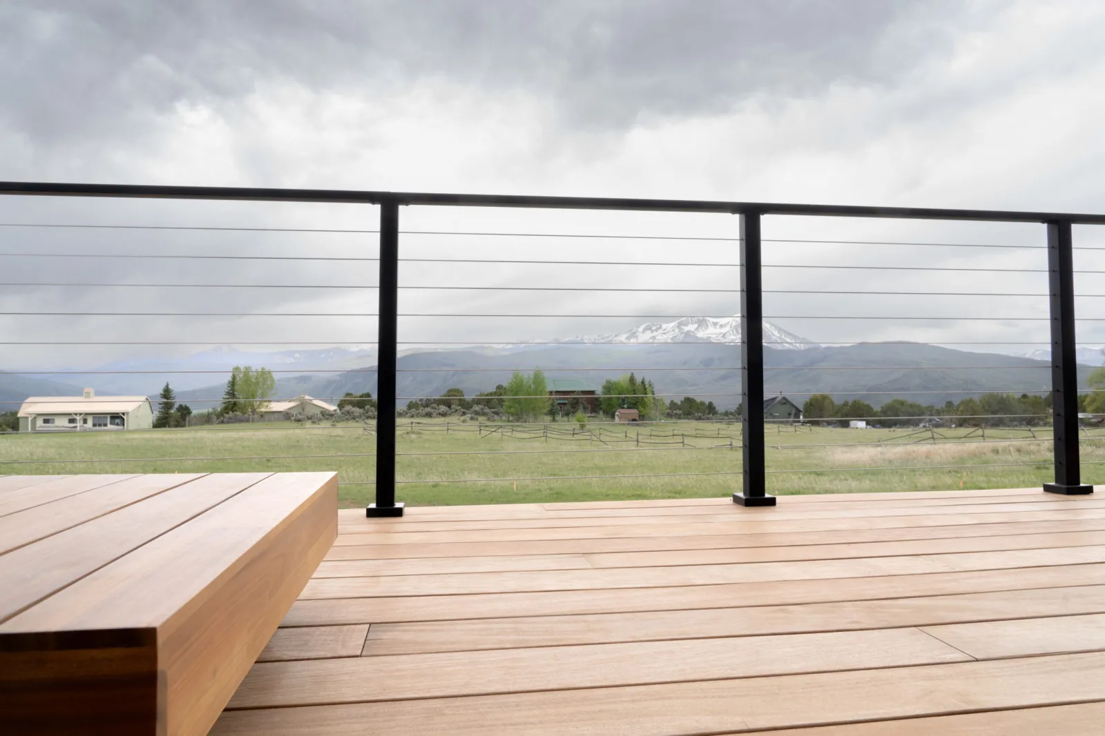 Deck seating with a wood bench and cable railing framing a snow-capped peak