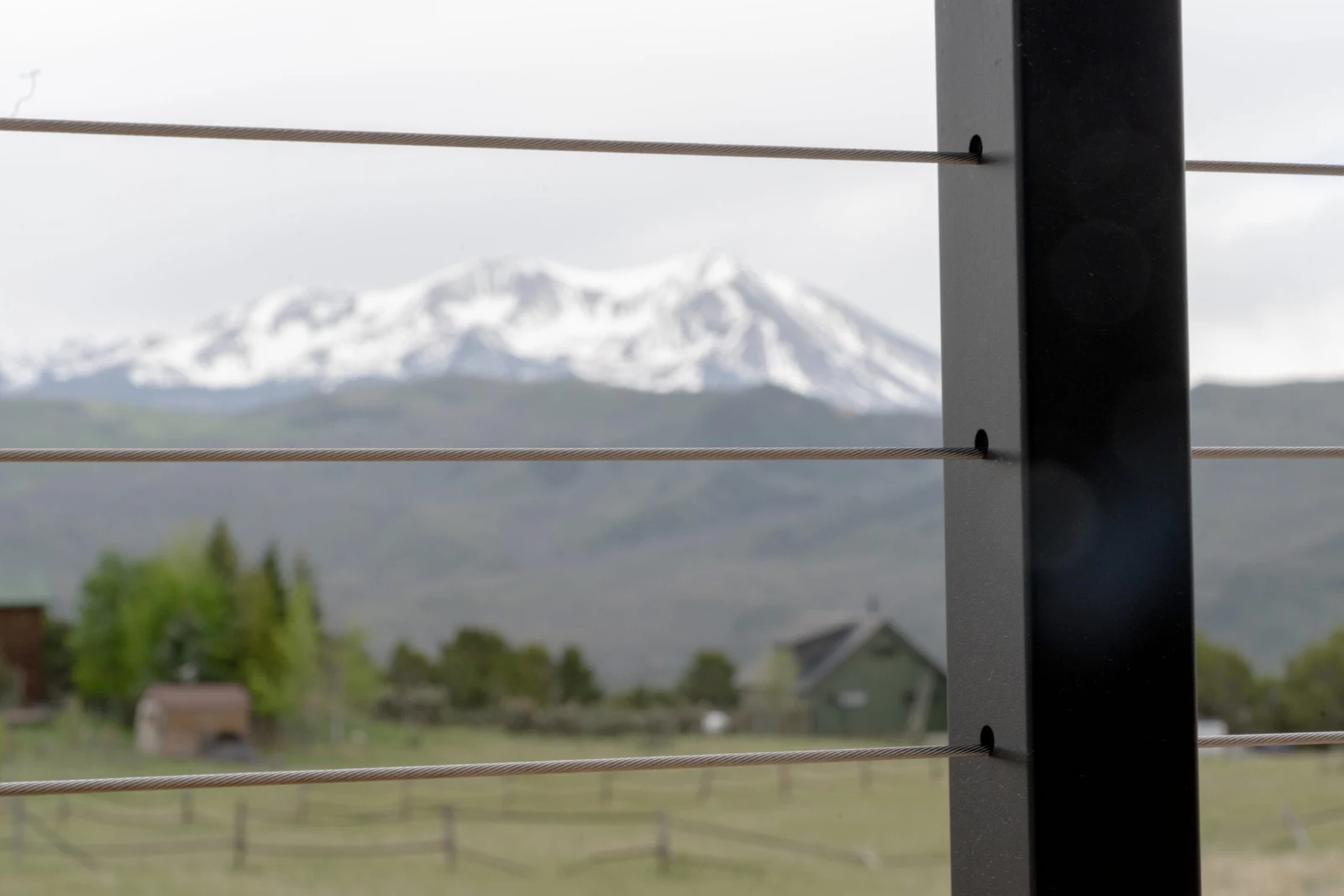 Black post in sharp focus with cables running toward a snow-capped mountain