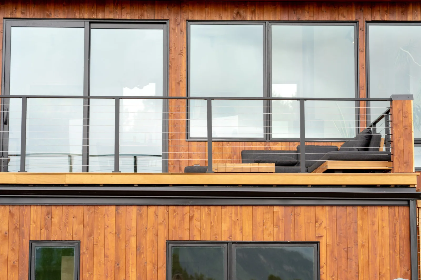 Long balcony run of black cable railing across the wood siding of a two-level facade
