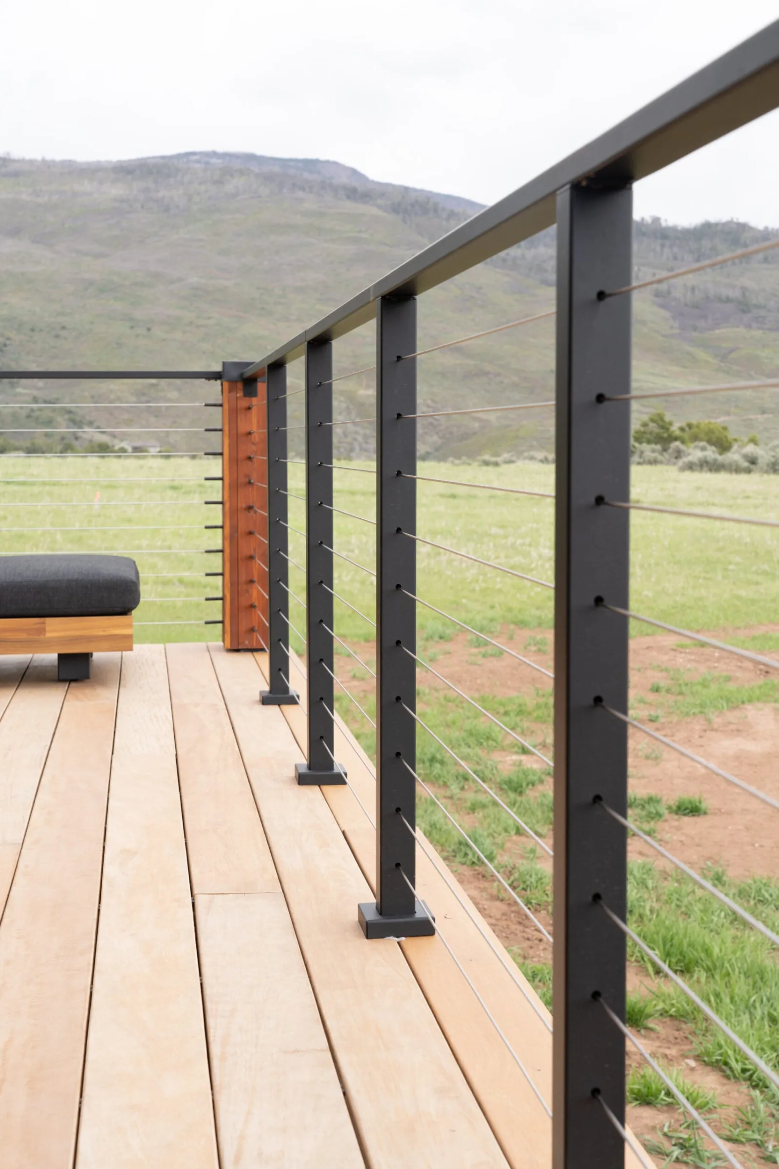 Deck looking down the railing line with black posts and taut cables over pasture