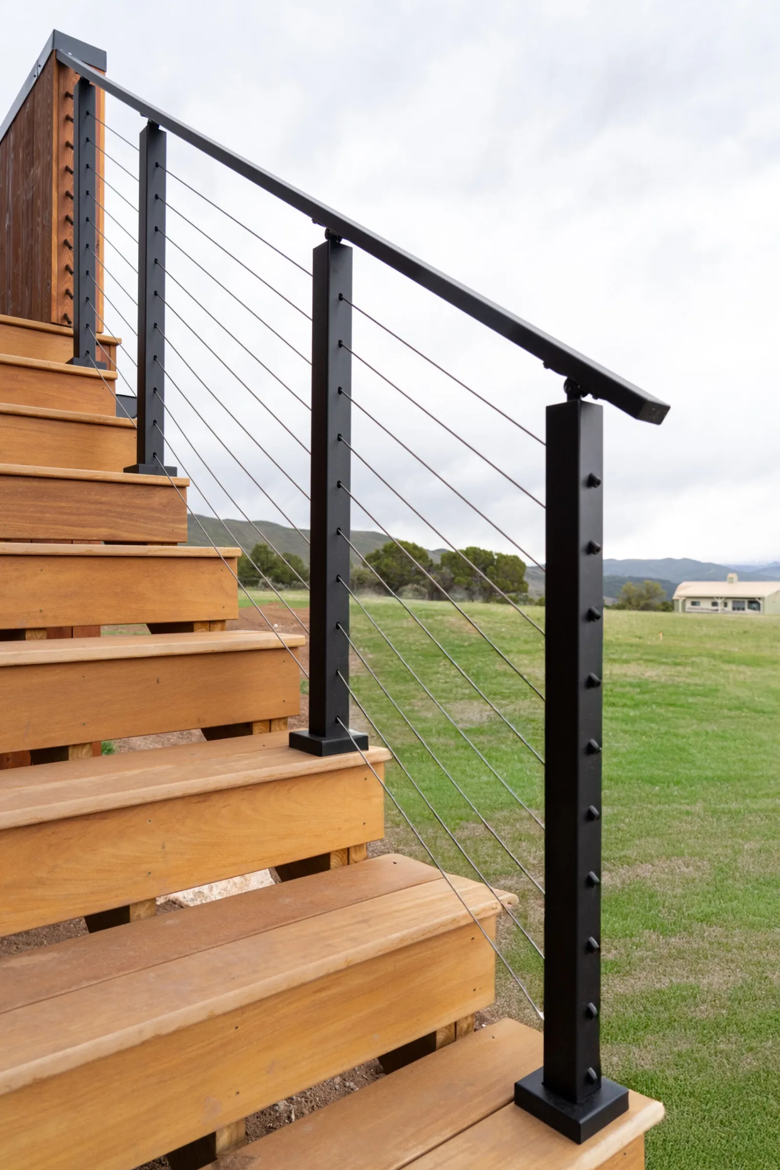 Cable railing climbing the outdoor stair run beside the lawn under gray sky