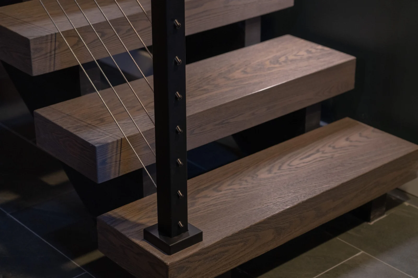 Wood treads beside a black post with cables running down to the slate floor