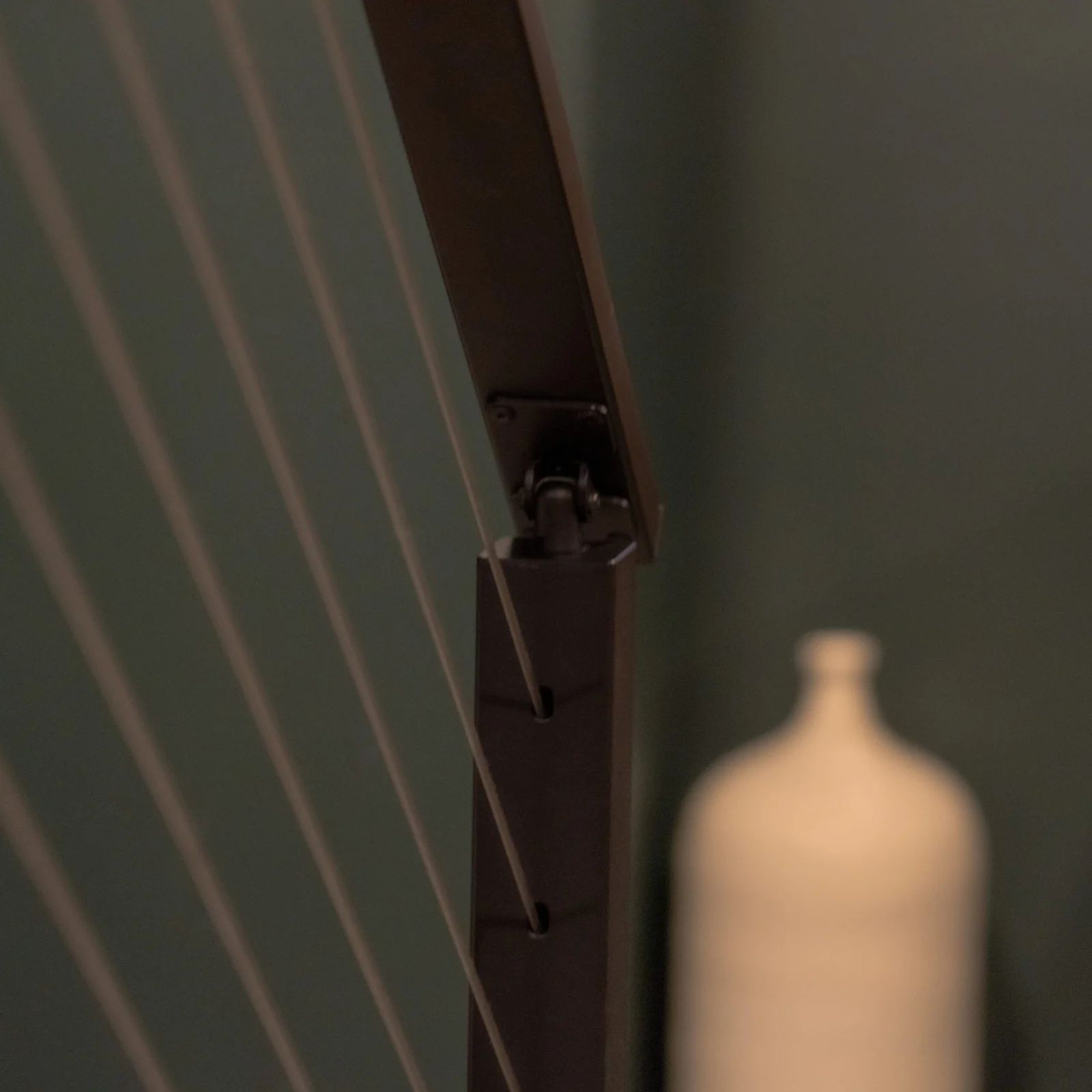 Dark top rail and post carrying taut cables beside a pale ceramic vessel