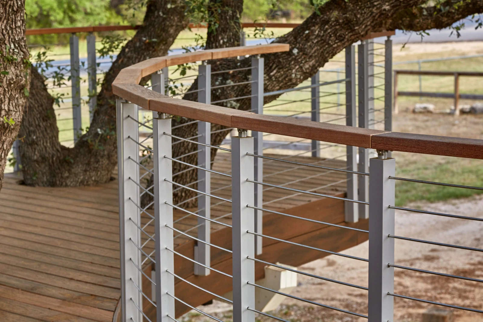 Curved wood handrail sweeping along the deck edge above evenly spaced stainless rods