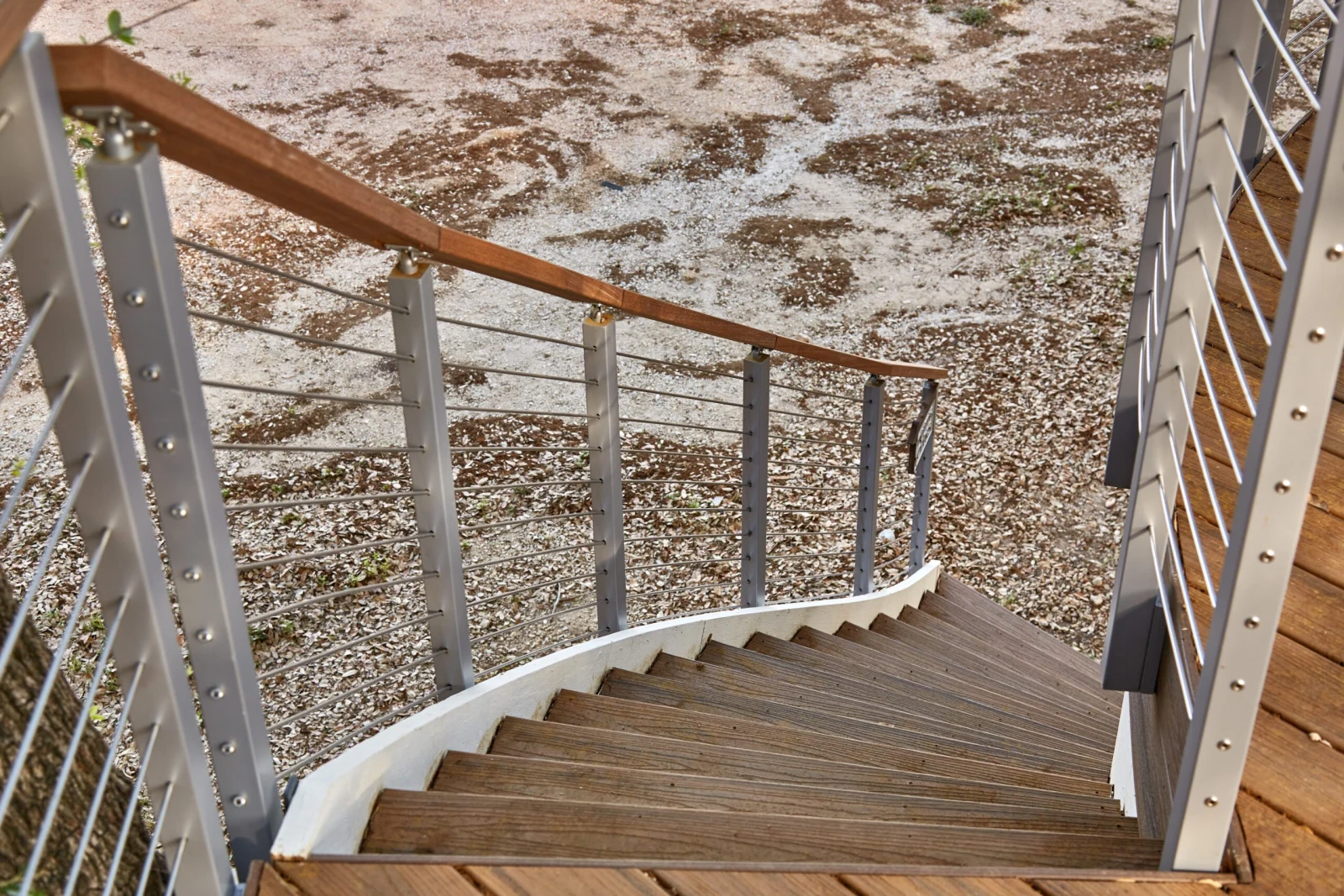Looking down a curving stair with rod railing on both sides over gravel