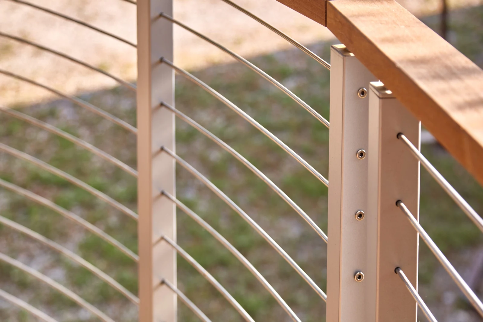 Close view of stainless rods passing through gray posts under a wood top rail