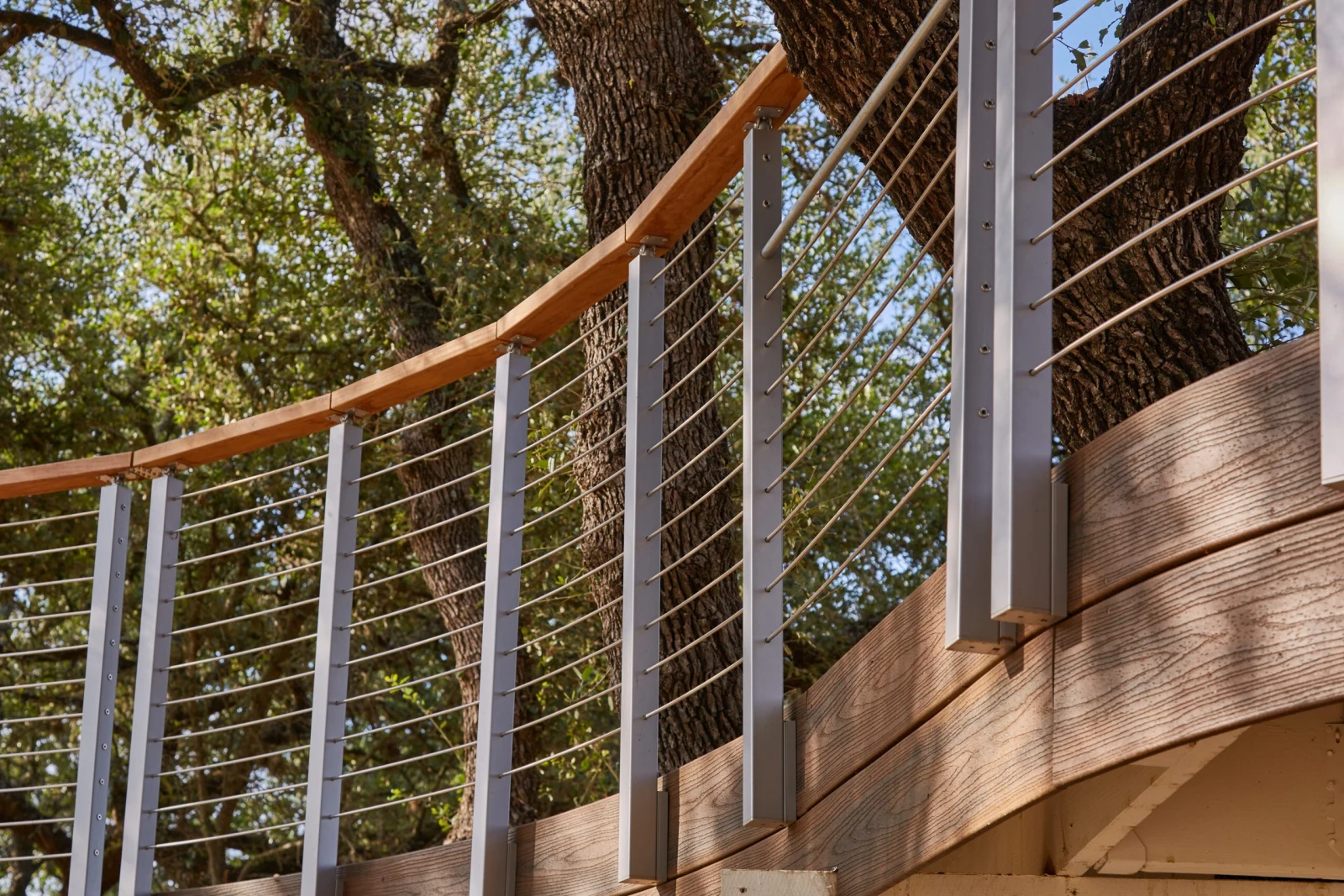 Upward view of deck railing posts and curved handrail against the tree canopy