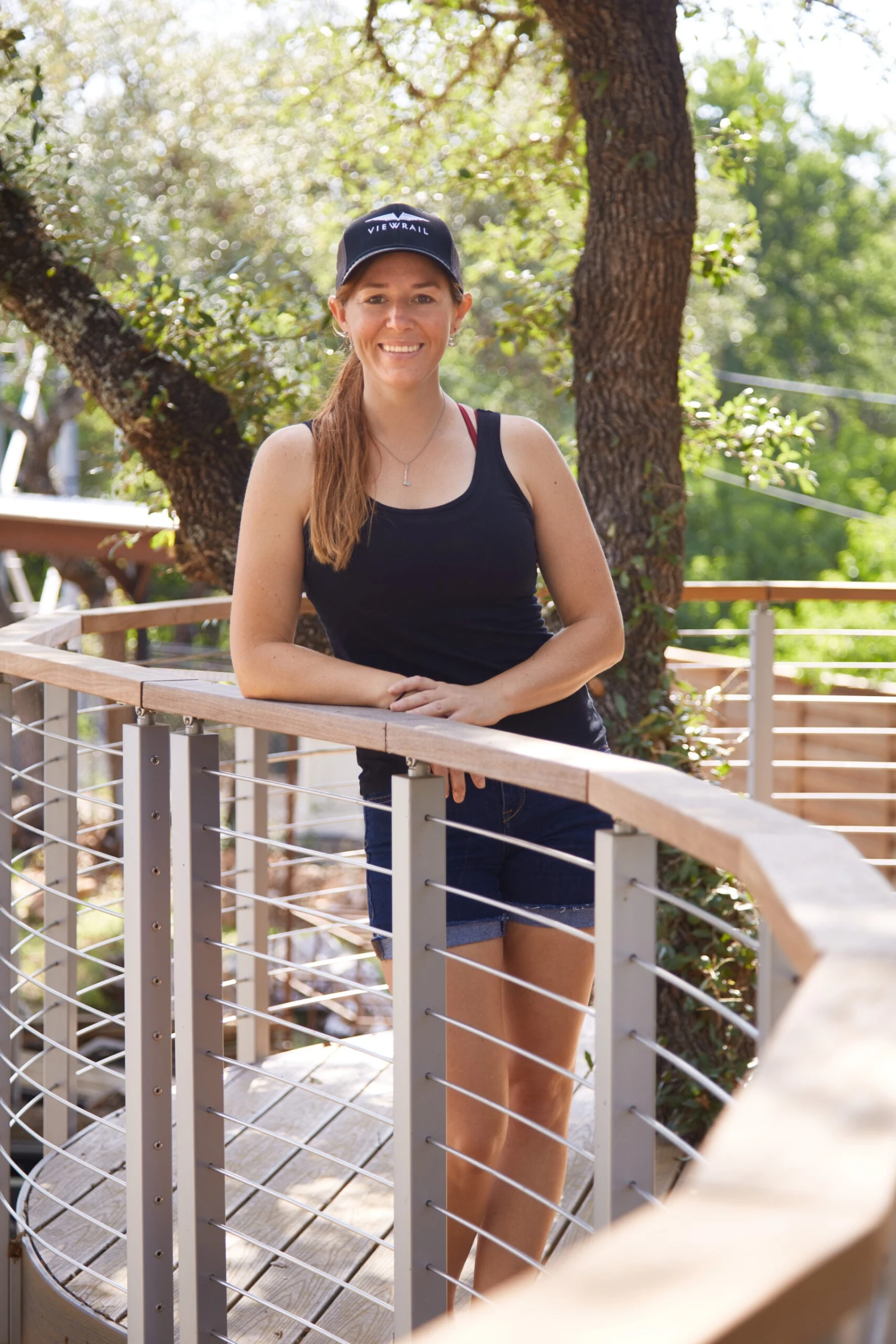Person leaning on the curved top rail of a raised deck among shade trees