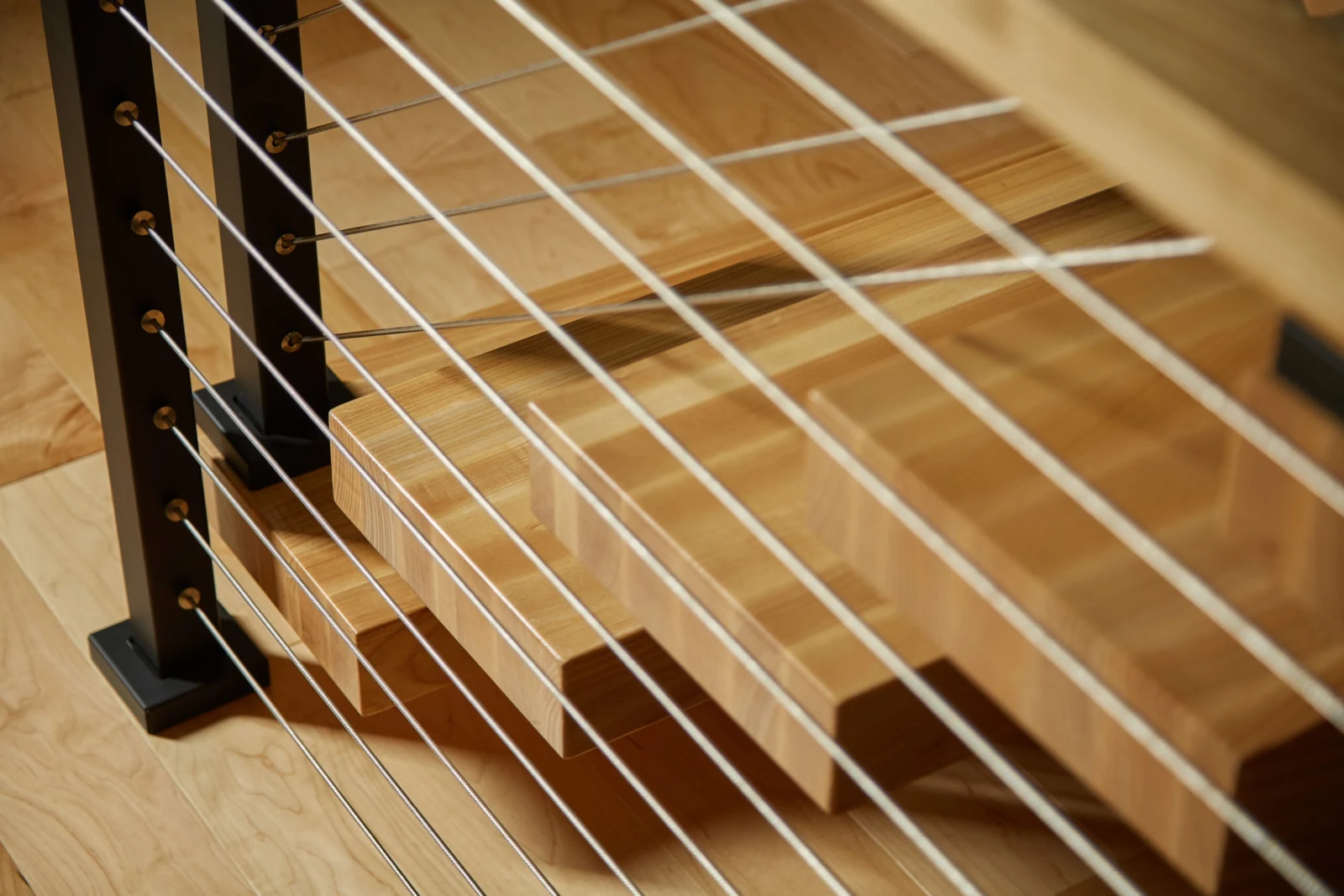 Close view of cable infill crossing light wood treads and a black post