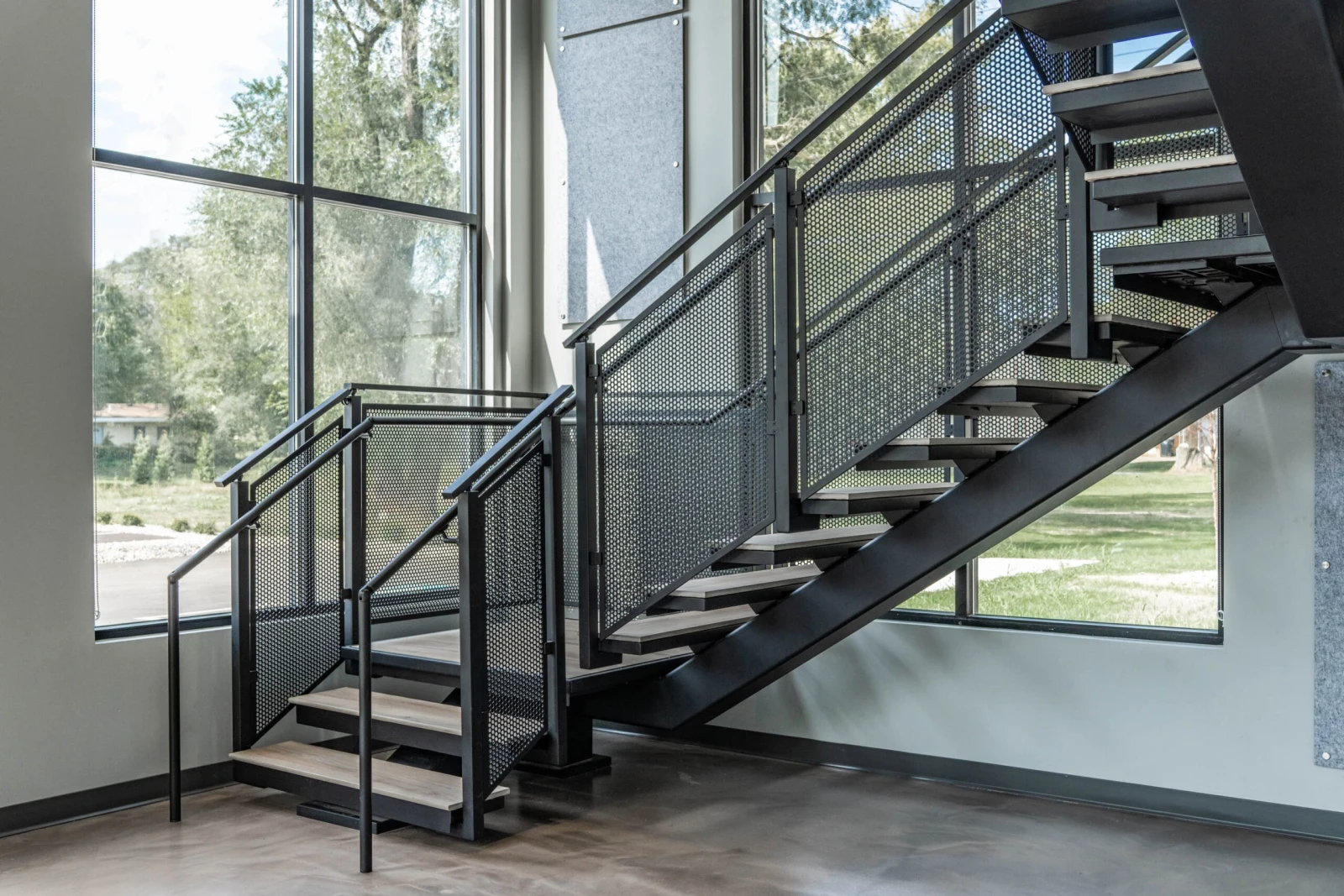 Black steel stair with perforated metal infill panels against a wall of tall windows