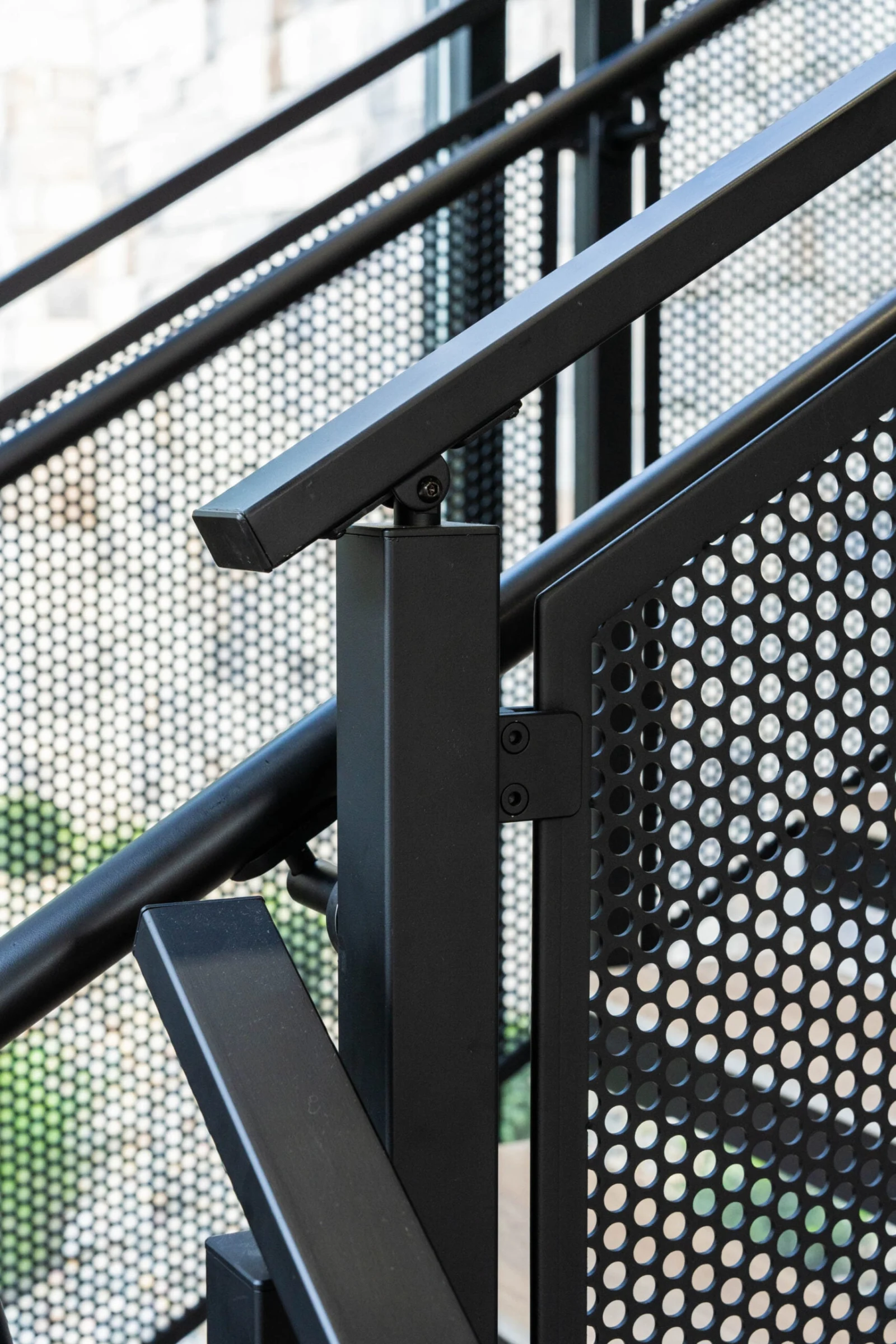 Detail of the square black post meeting the top rail beside perforated infill