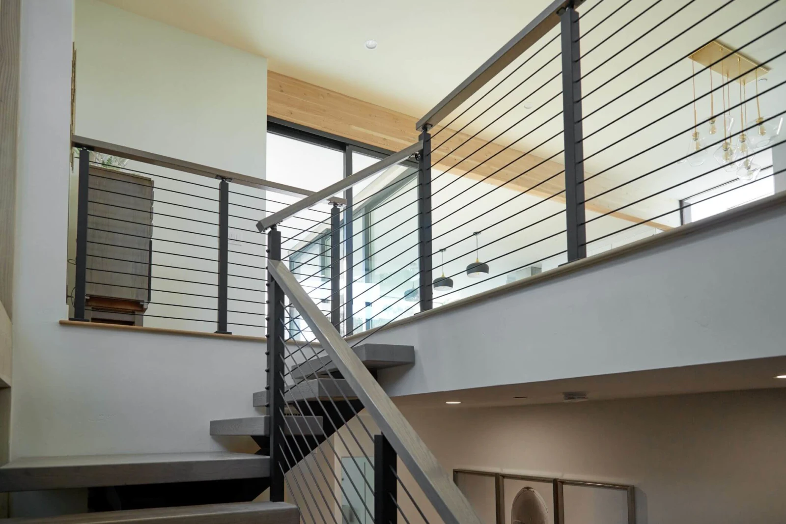Black rod railing lines a balcony and stair below a wood ceiling and brass chandelier