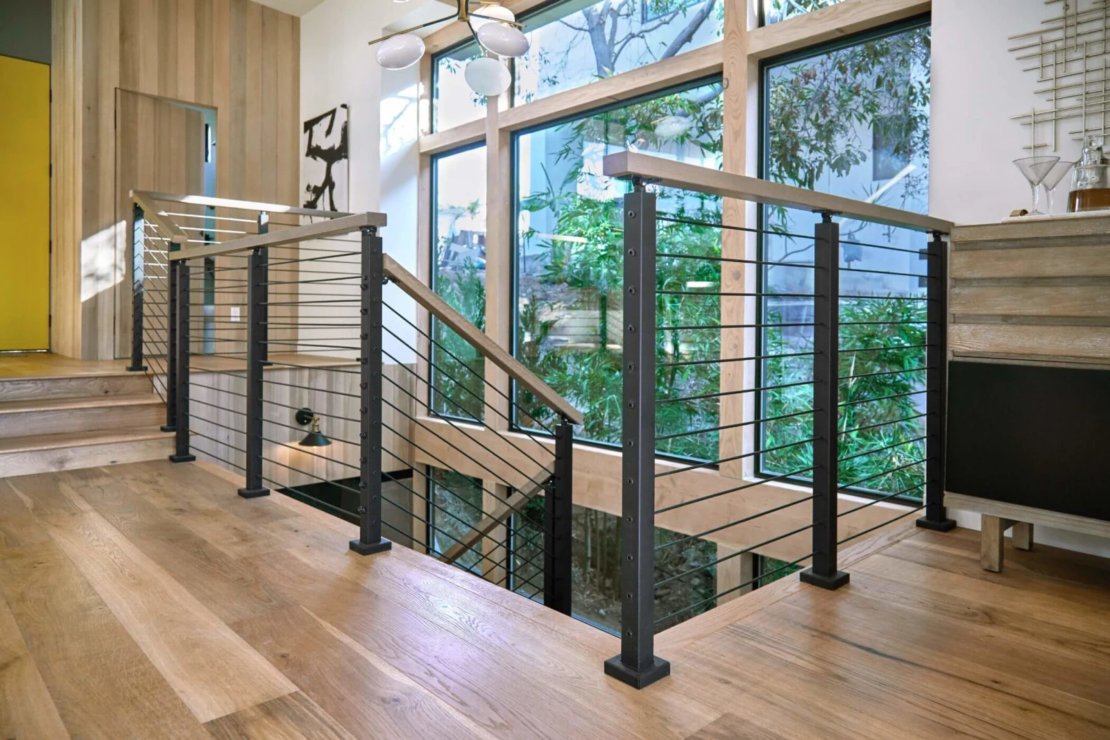 Rod railing wrapping a stairwell opening in a bright room with tall windows