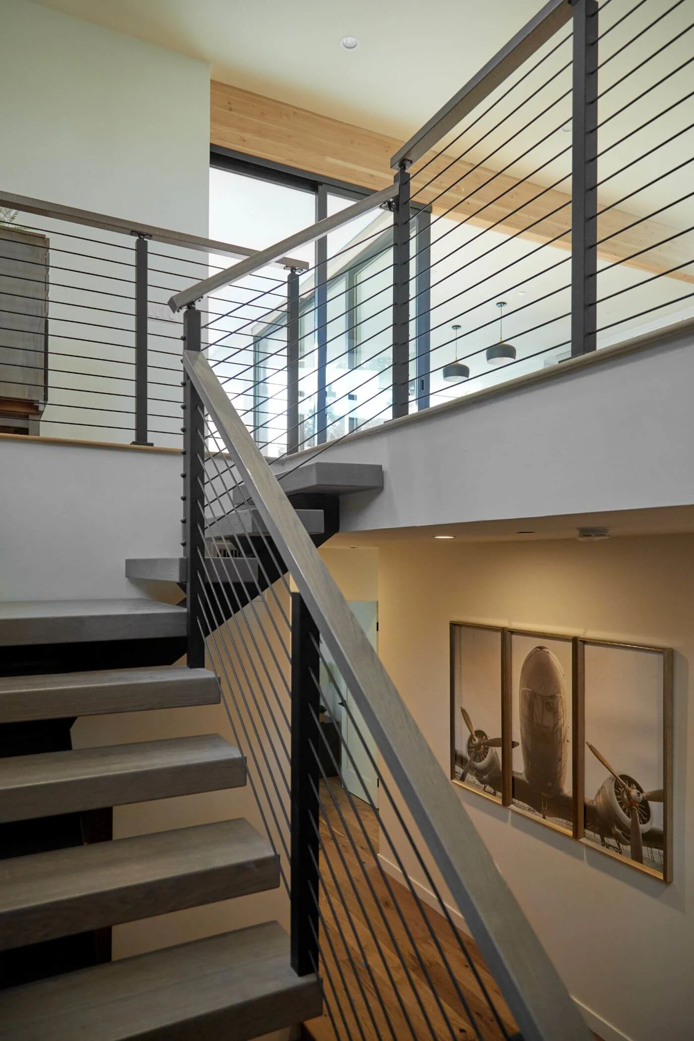 Stairwell with pale treads climbing past artwork behind a run of rod railing